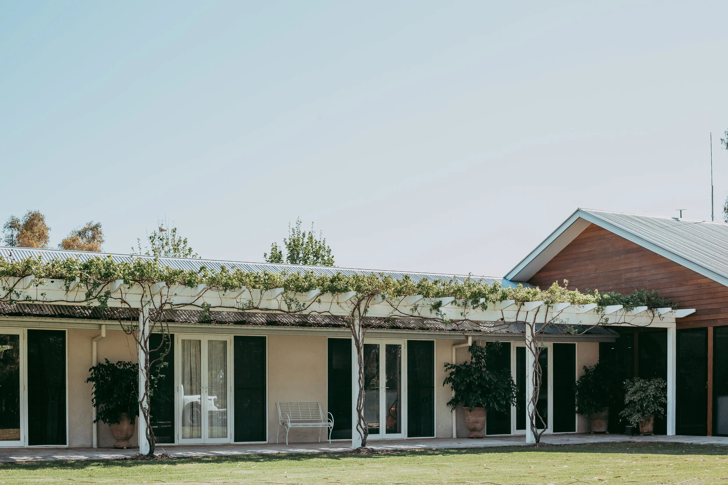 Single-story house with veranda, plants, and a metal roof under a clear sky.