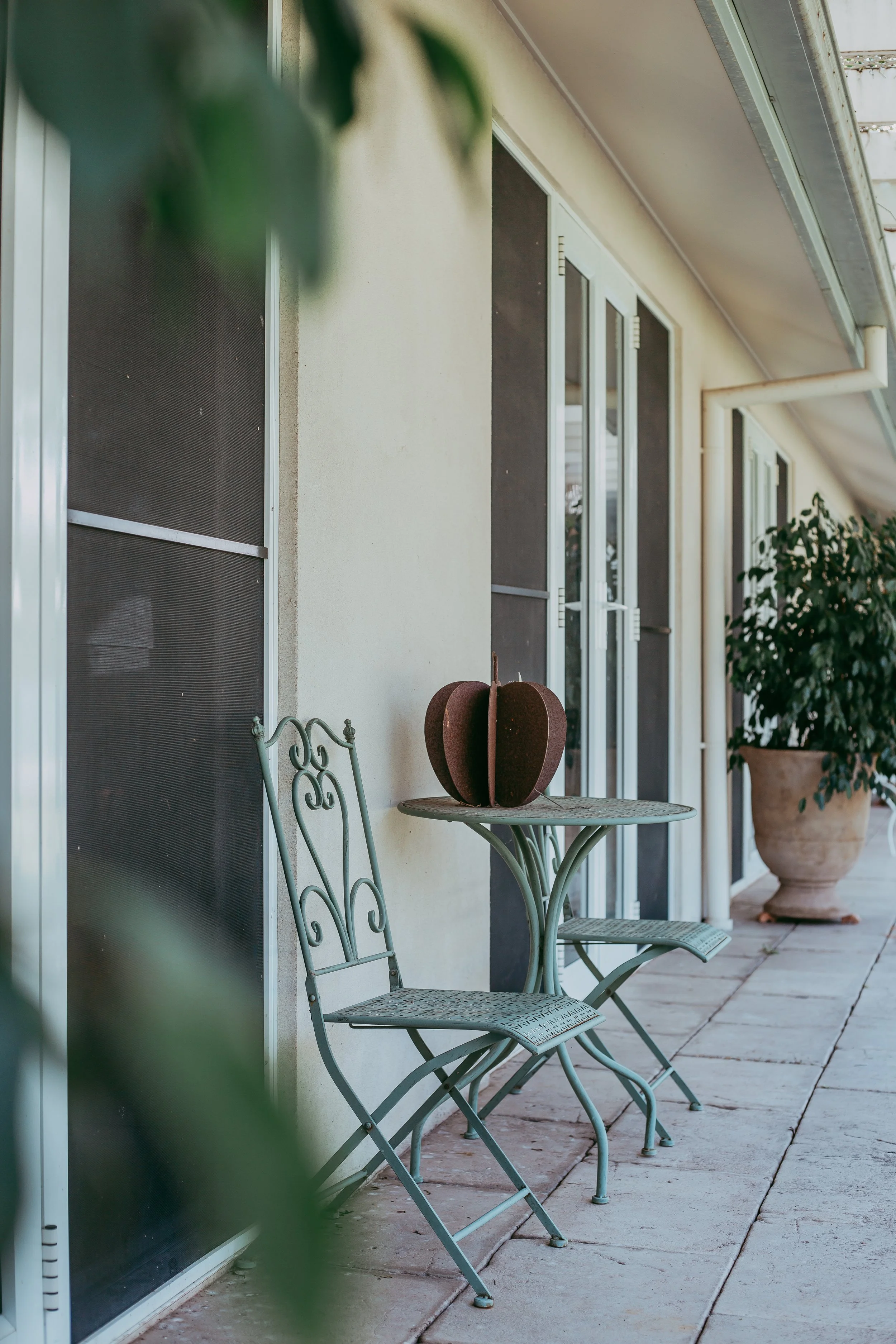 Outdoor patio with metal chairs, a small table with a decorative object, and potted plant by a building wall.