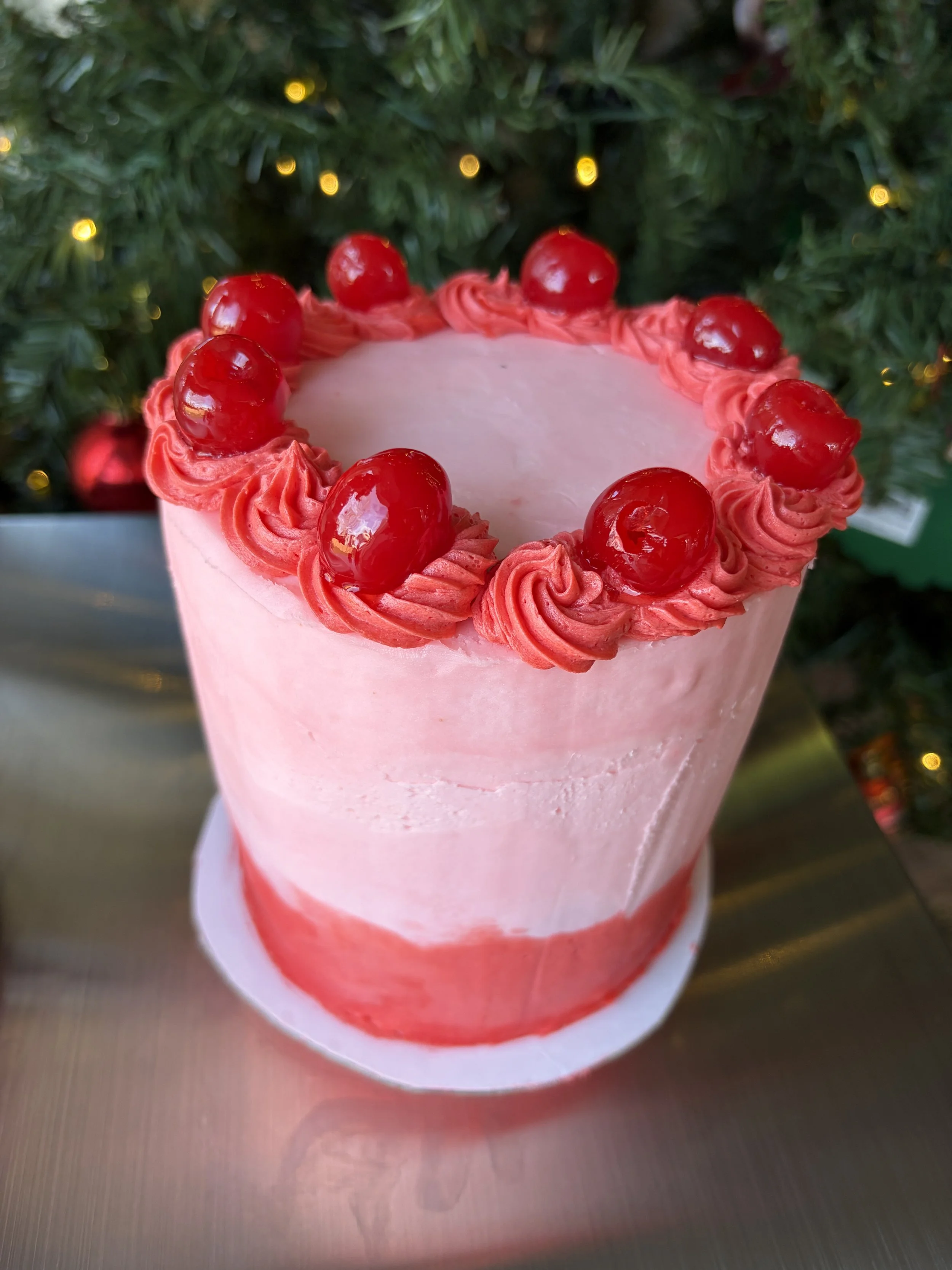 A two-toned pink cake topped with dark pink buttercream swirls and red cherries.