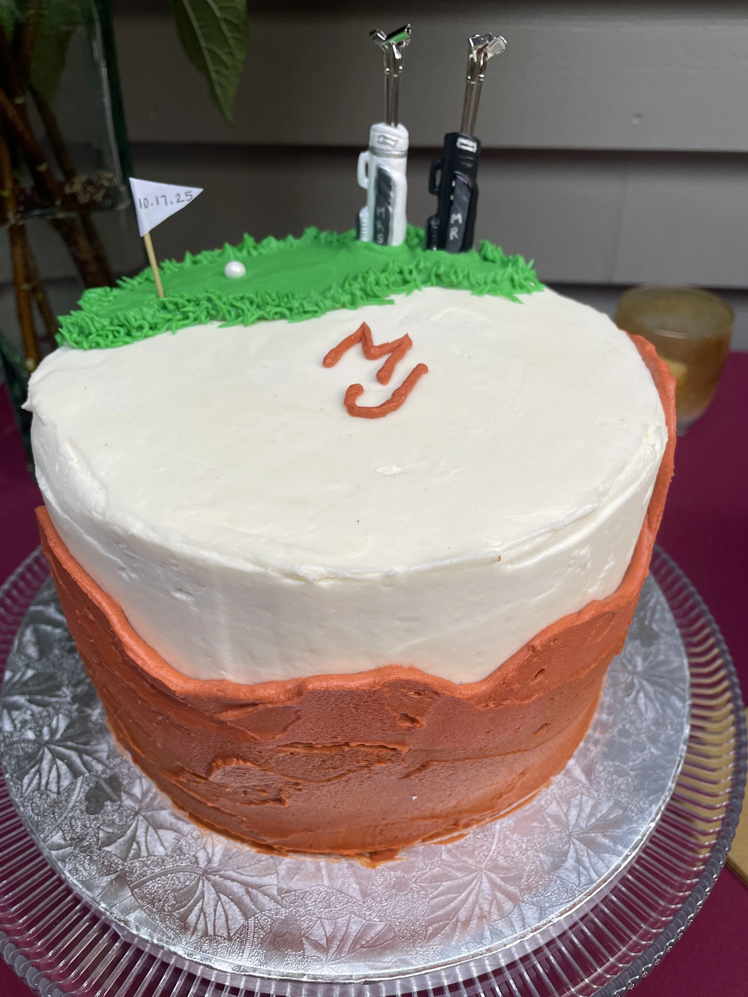 White cake with orange detailing. Green buttercream on top made to look like miniature golf course with bridal golf clubs.