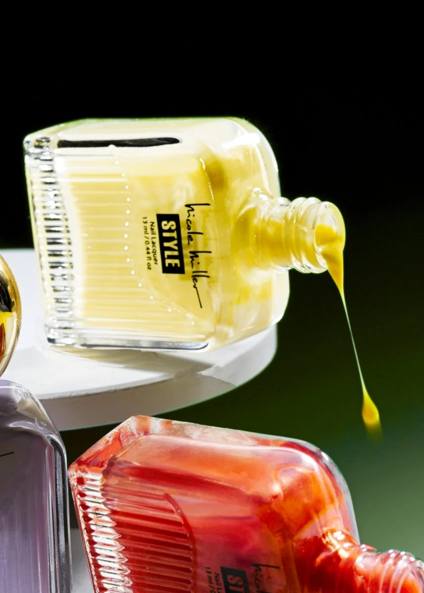 Close-up of colorful nail polishes in glass bottles, yellow and red, on a white surface against a black background.