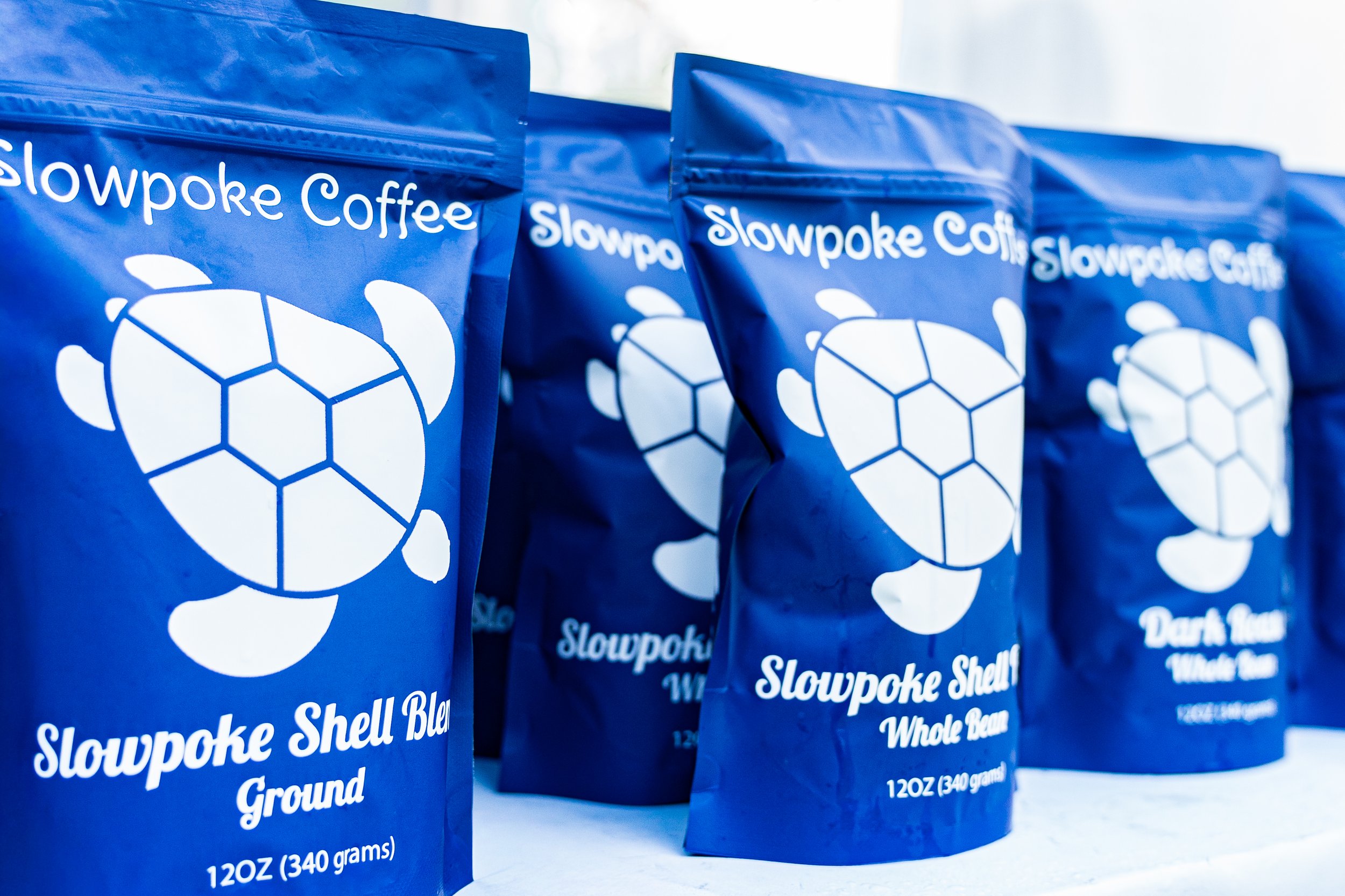 Multiple blue bags of Slowpoke Coffee Ground Whole Bean arranged in a row on a white surface.