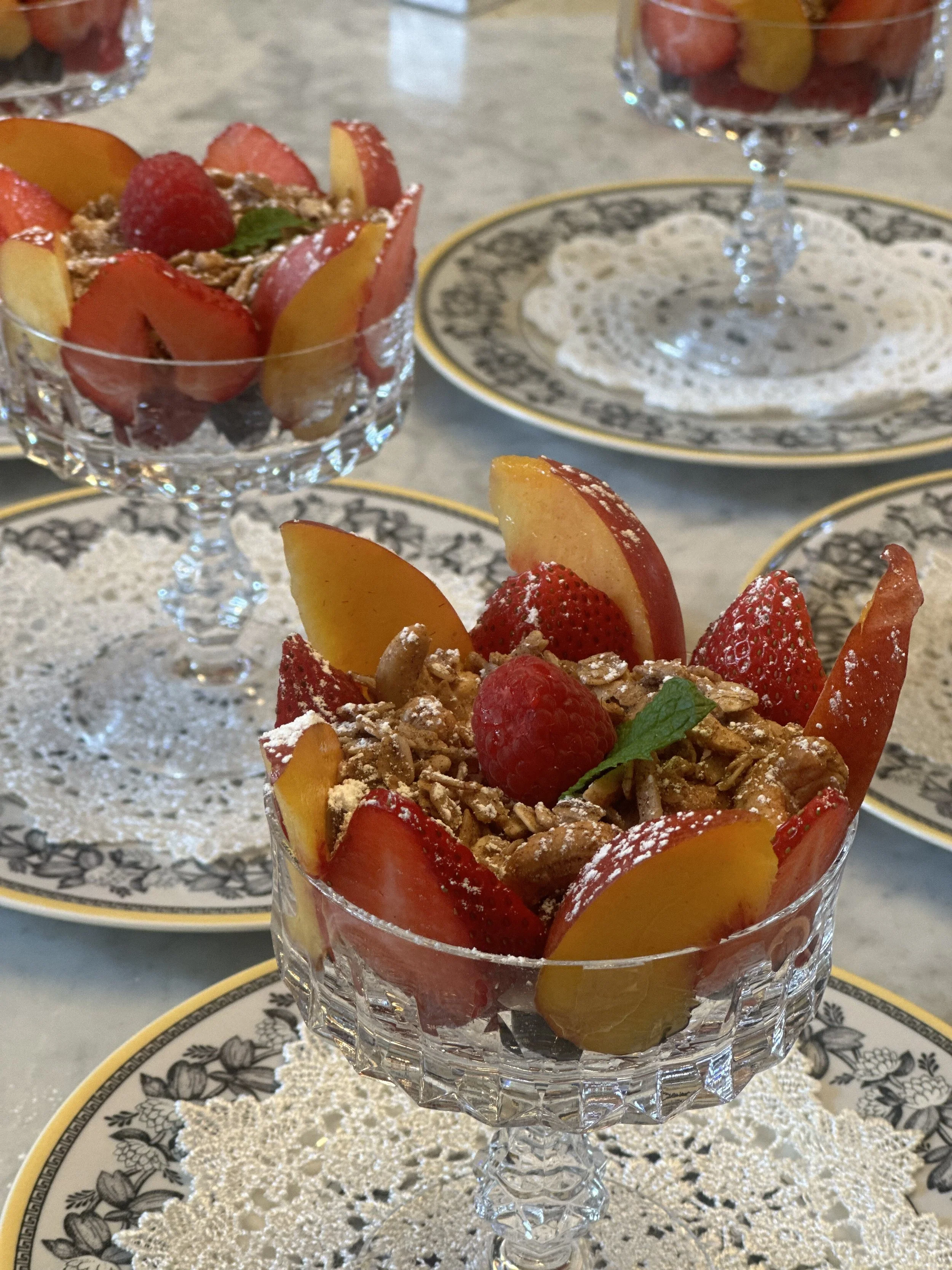 Fruit parfaits with strawberries, peaches, raspberries, granola, and mint in crystal glasses.