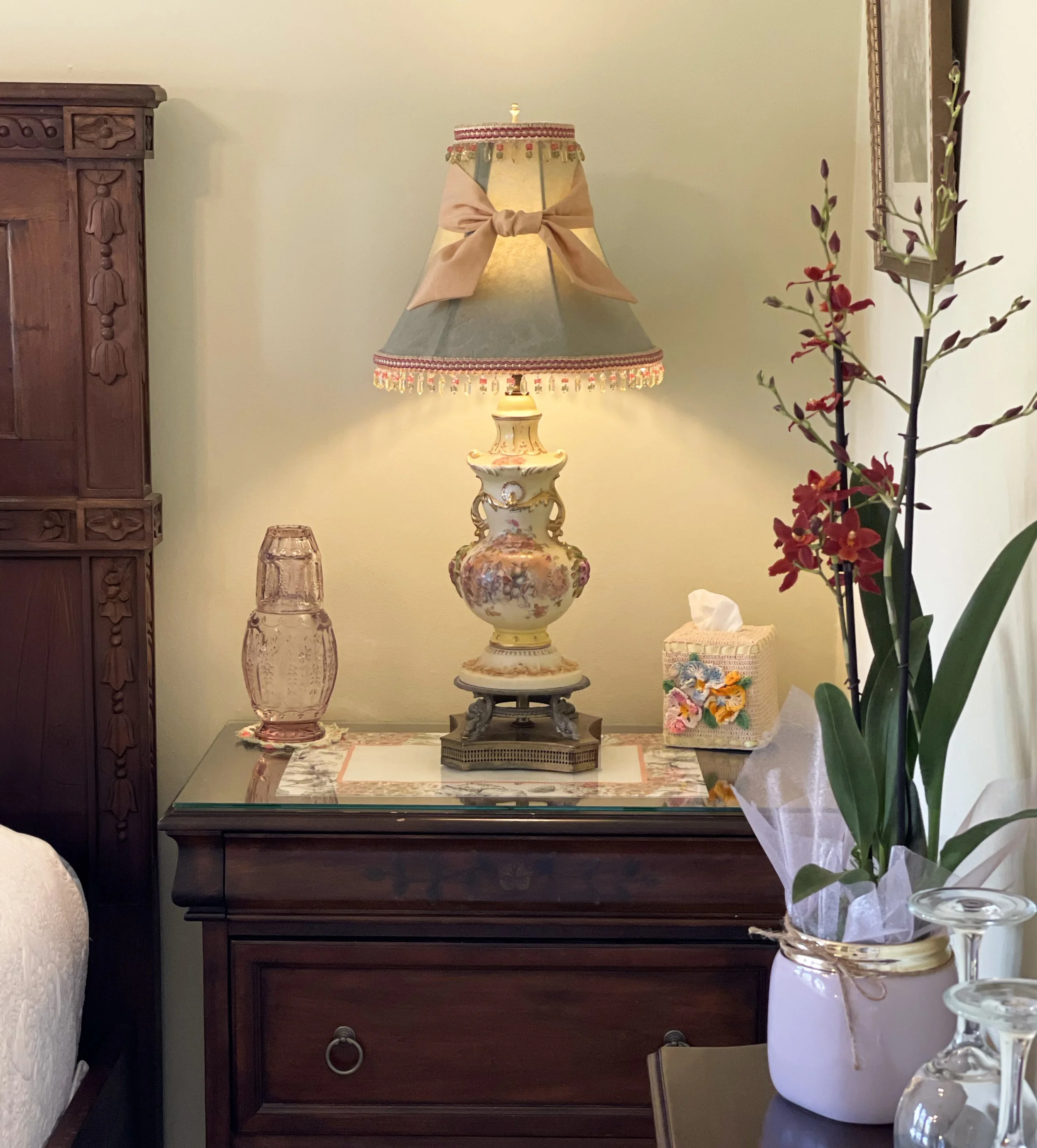 Bedroom nightstand with a vintage lamp, decorative vase, tissue box, and floral arrangement.