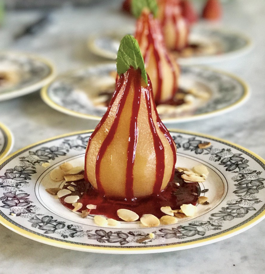 Poached pear dessert with red sauce, garnished with mint and sliced almonds on decorative plates.