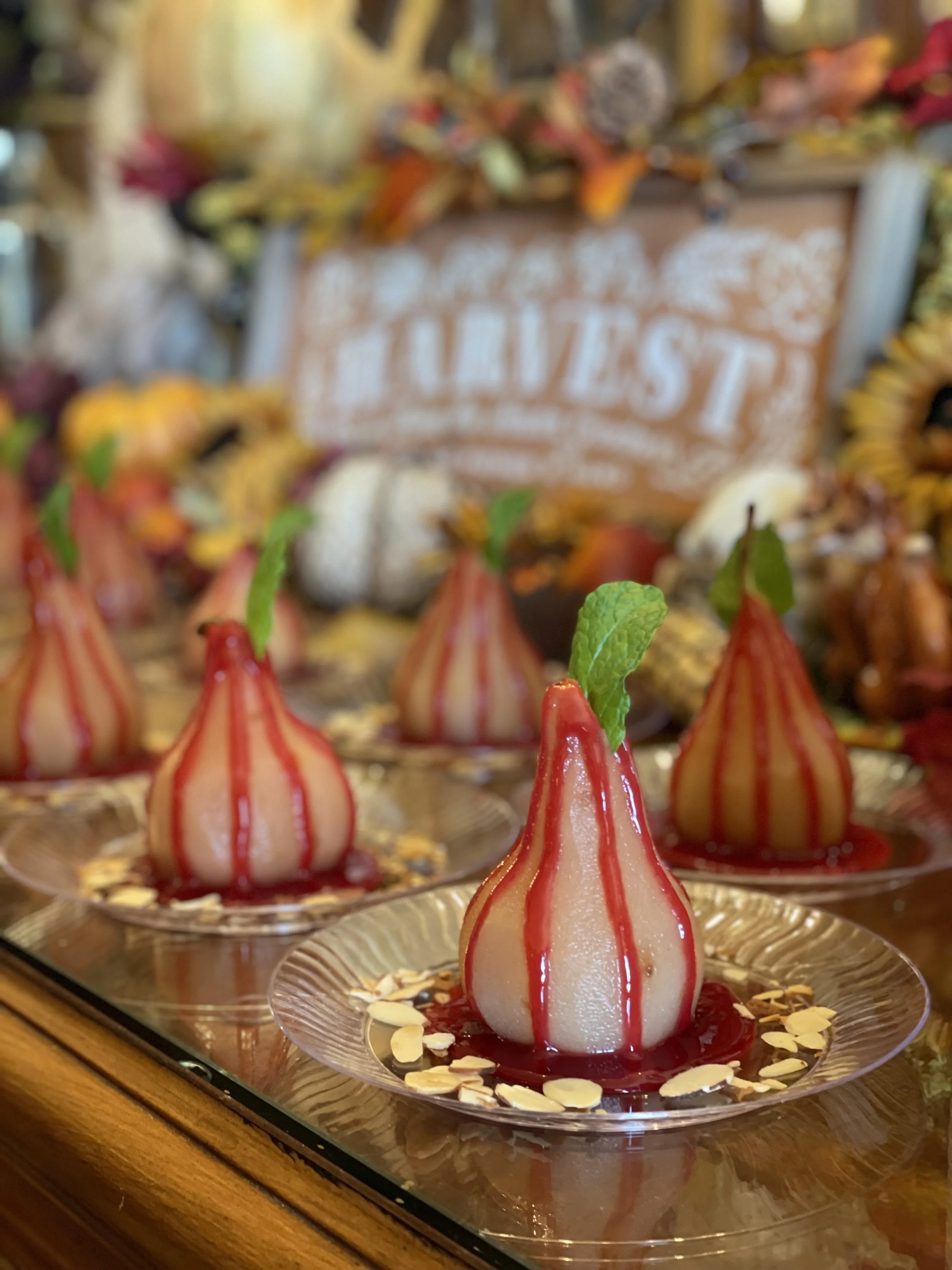 Poached pears with red sauce on clear plates, garnished with mint leaves and sliced almonds, in a harvest-themed setting.