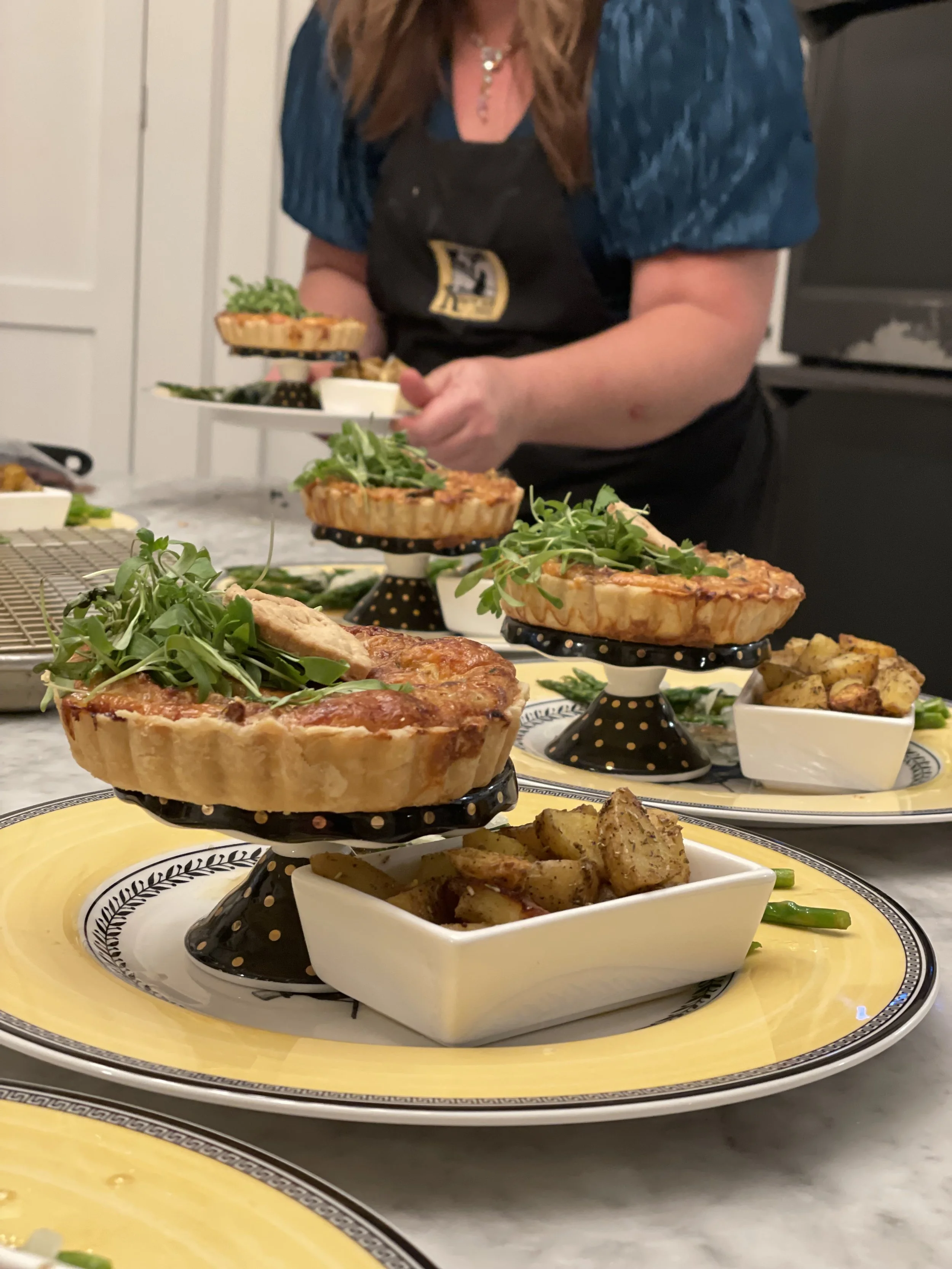 Quiche and roasted potatoes served on decorative plates with a person arranging dishes in the background.