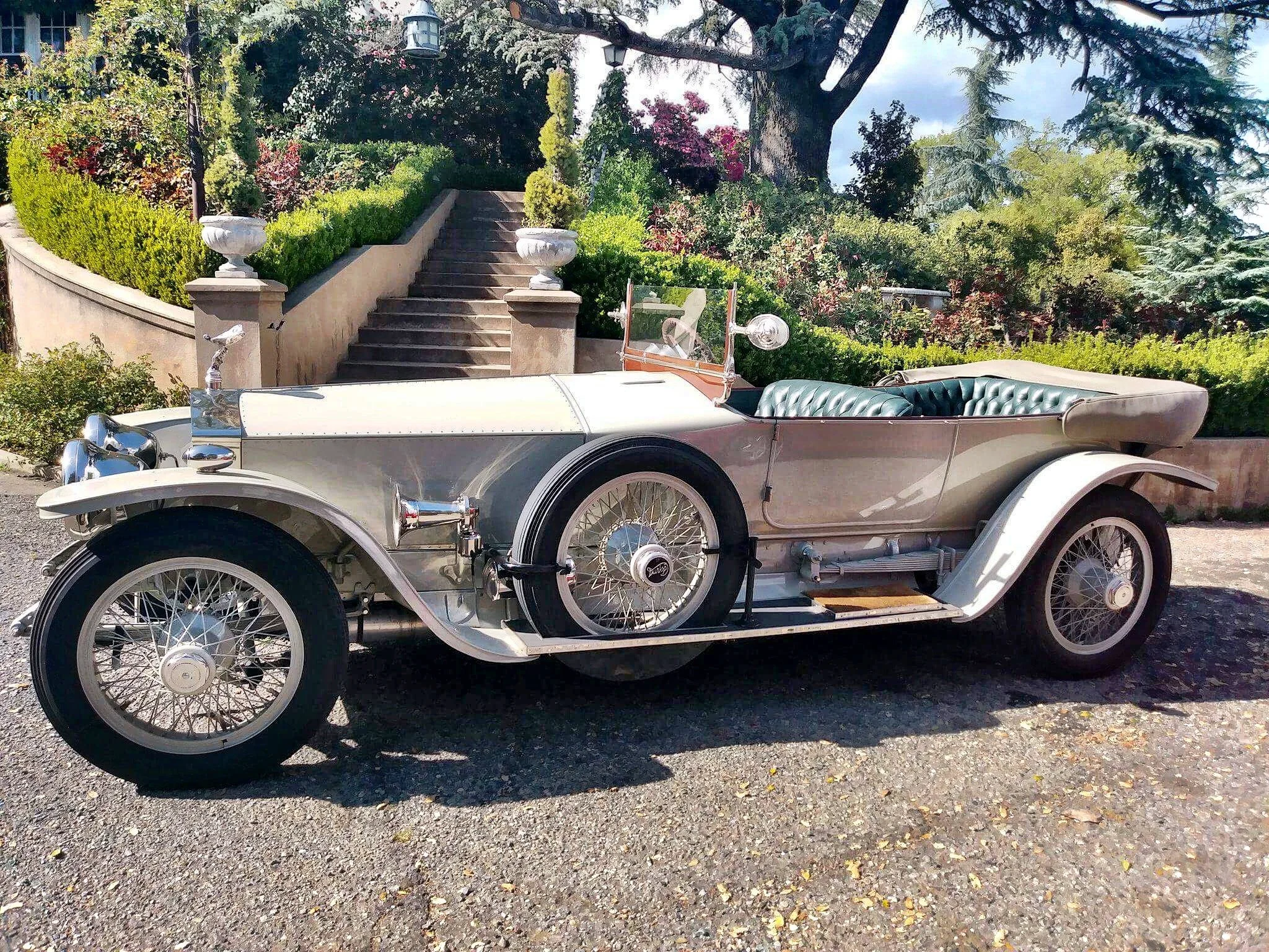 Vintage car parked in front of landscaped garden with stairs and greenery in the background.
