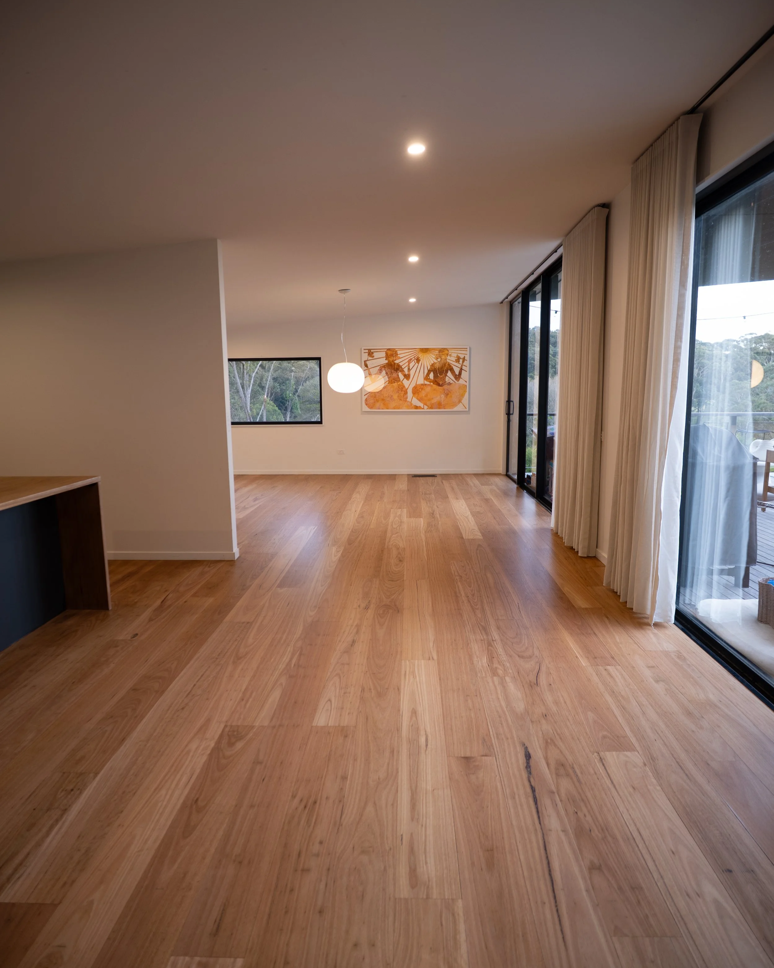 Room with wooden flooring, kitchen area with white cabinets and a ceiling fan.