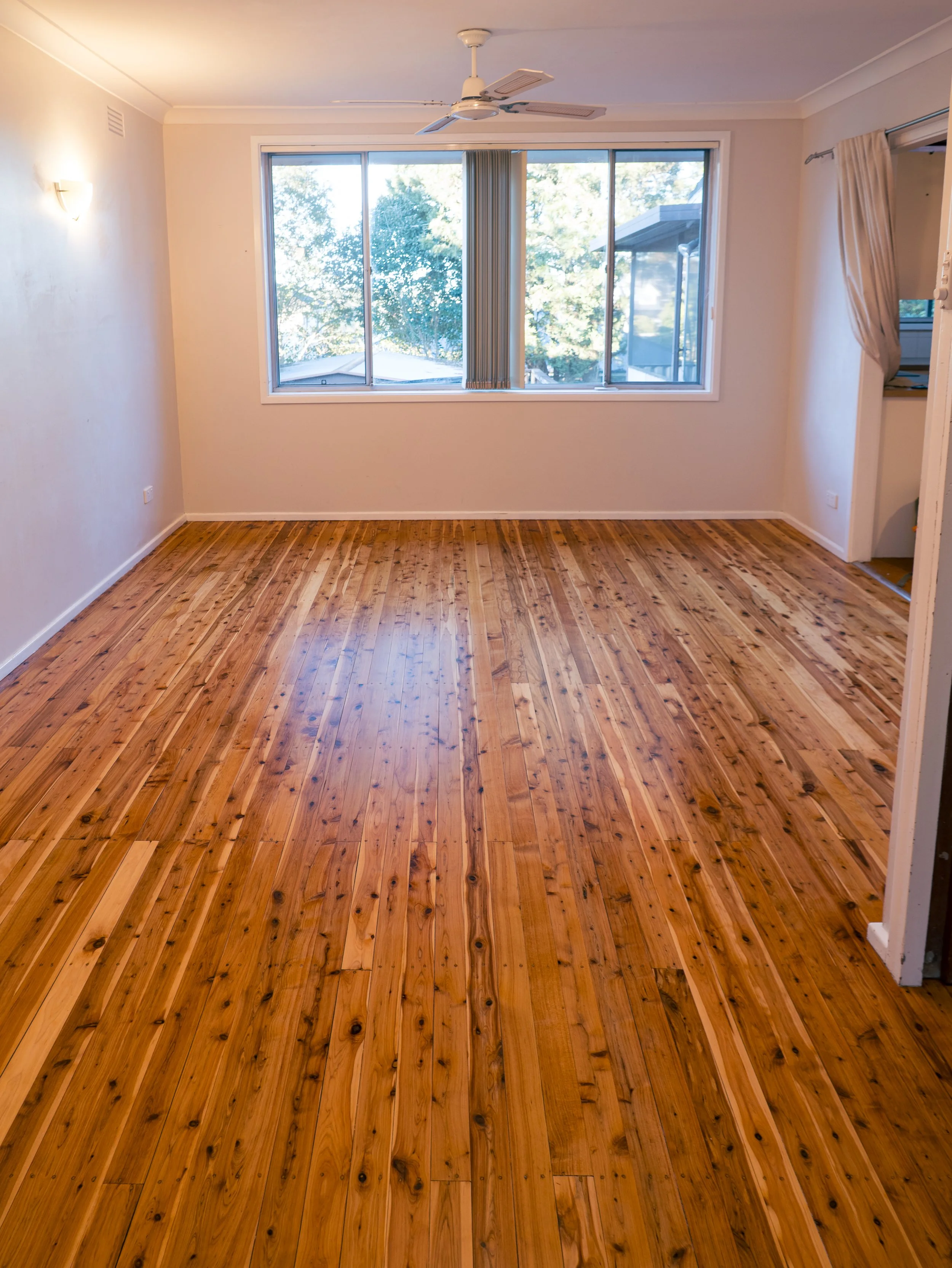 Modern empty living room with wooden floor, built-in cabinets, ceiling fan, and recessed lighting.