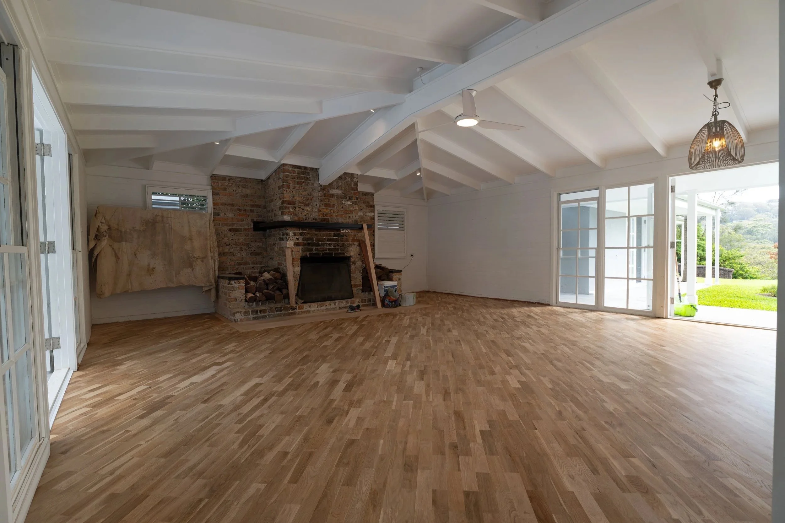 Room with wooden flooring, kitchen area with white cabinets and a ceiling fan.