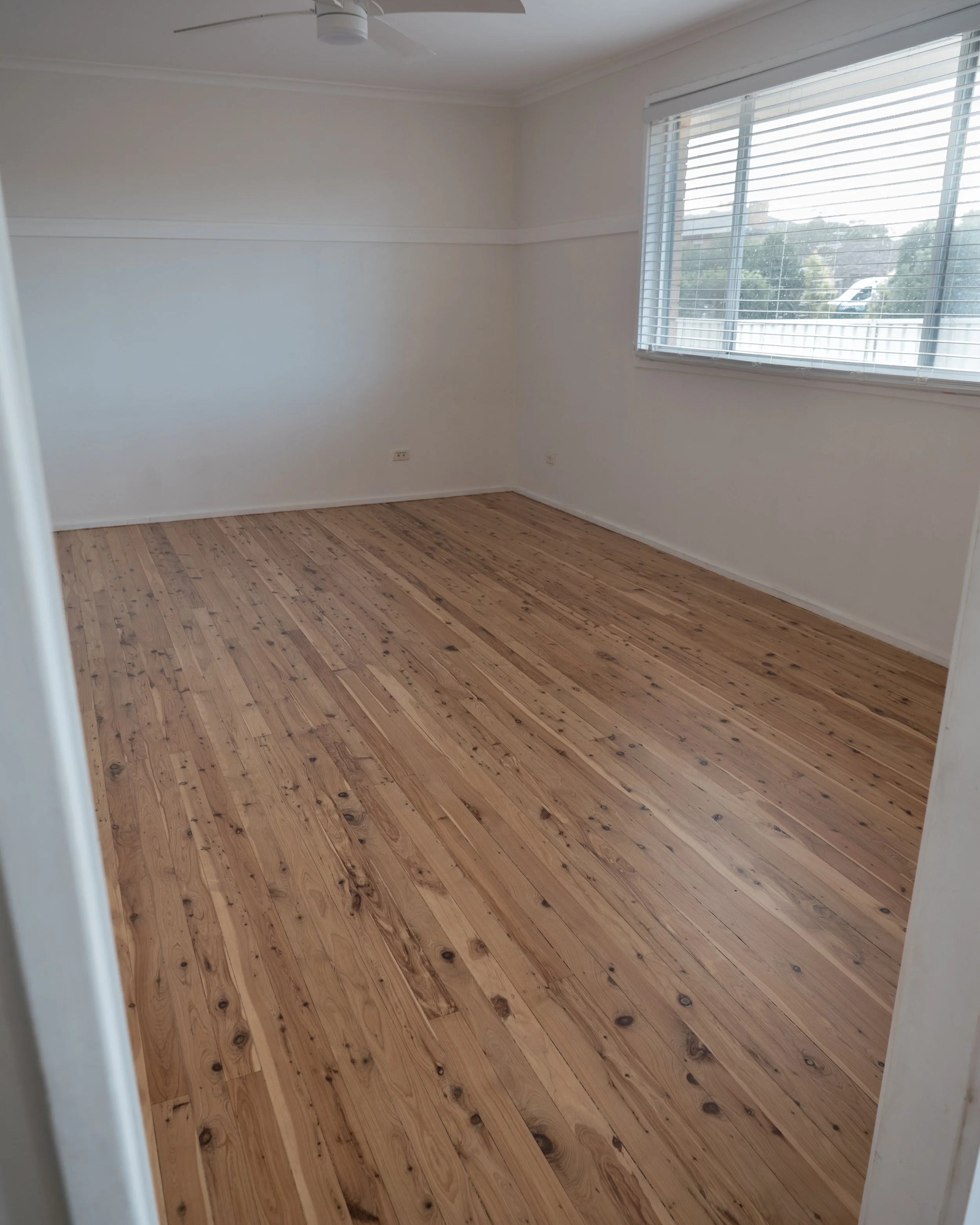 Modern empty living room with wooden floor, built-in cabinets, ceiling fan, and recessed lighting.