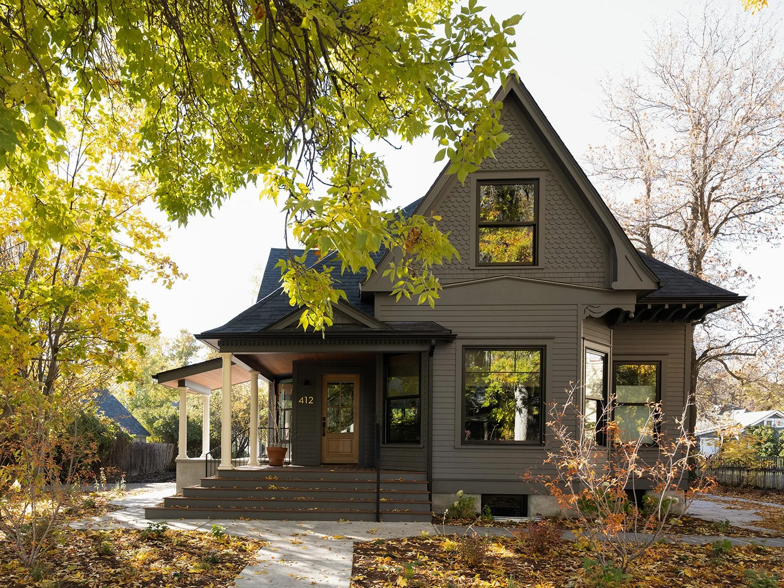 A gray two-story house with a front porch, surrounded by trees with autumn leaves, and steps leading to the front door. Bozeman, Montana, Remodel.