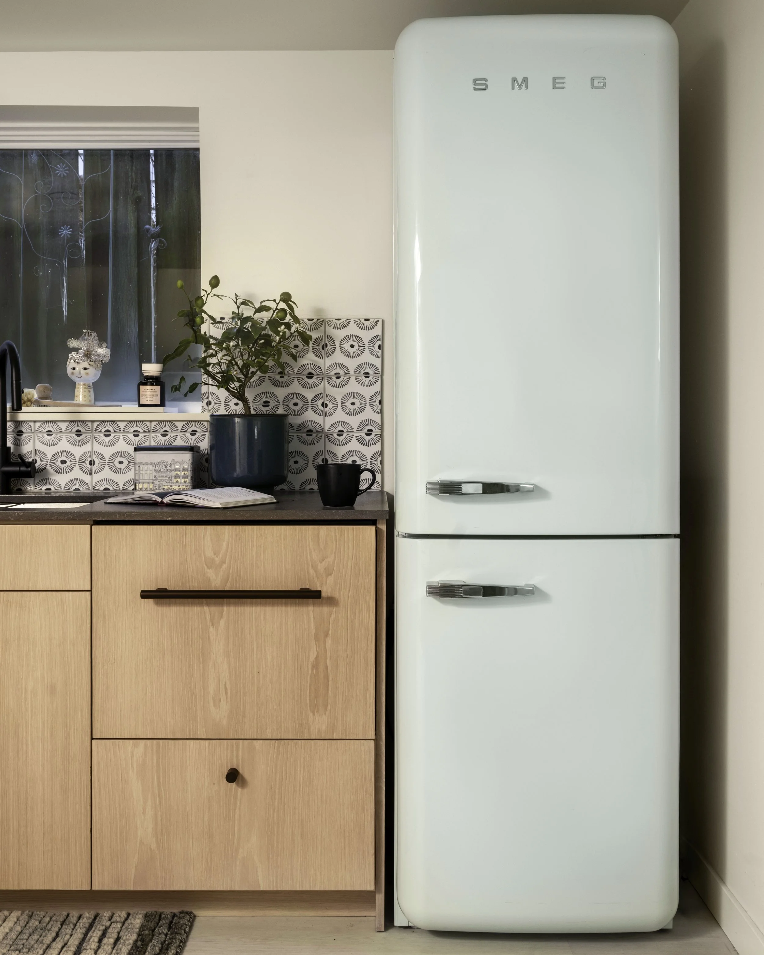 Cream-colored vintage Smeg refrigerator in a modern kitchen with wooden cabinets, a black faucet, potted plant, black mug, and kitchen window. Seattle, Queen Anne, Basement, Remodel.