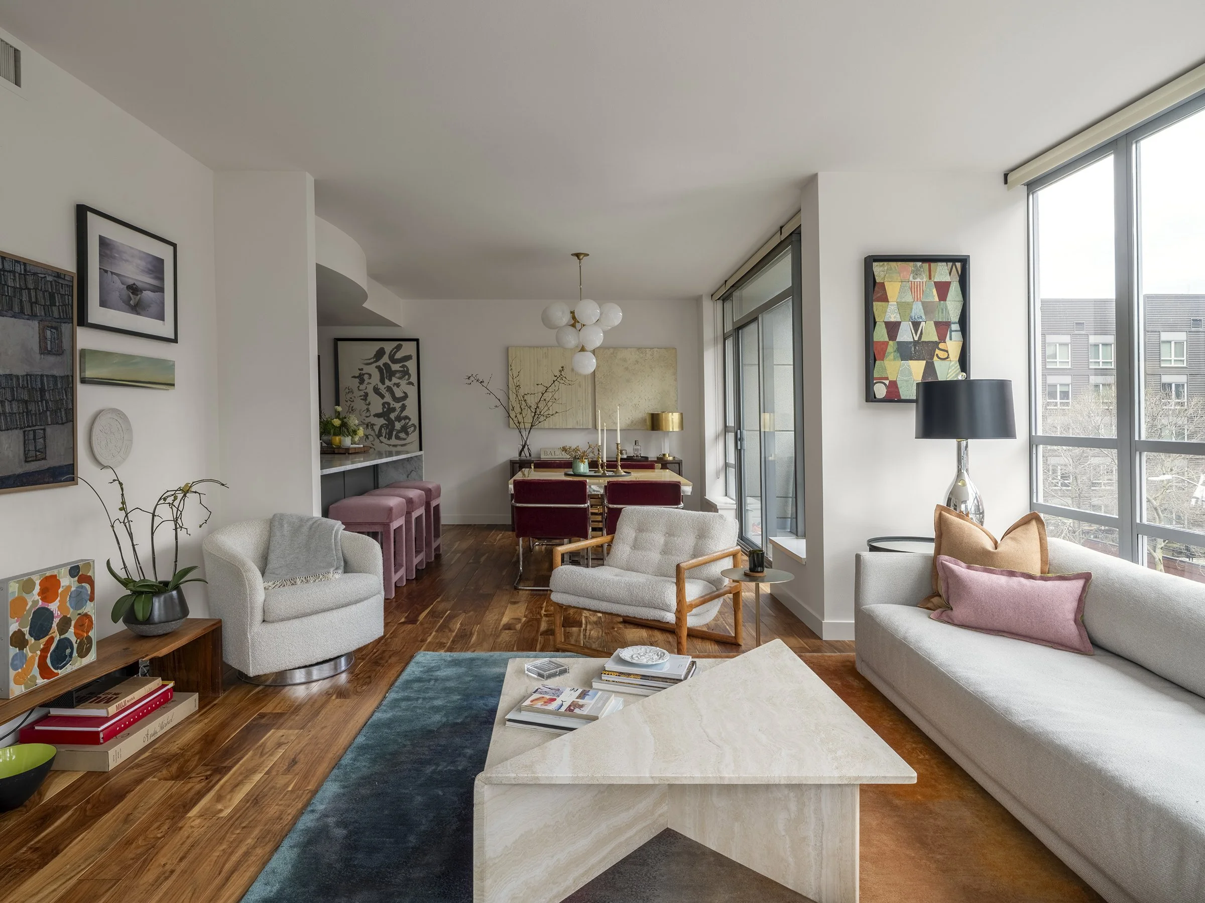 Bright living room with white sofa, armchair, colorful artwork, large windows, and hardwood floors. Seattle, Belltown, Condo, Remodel.