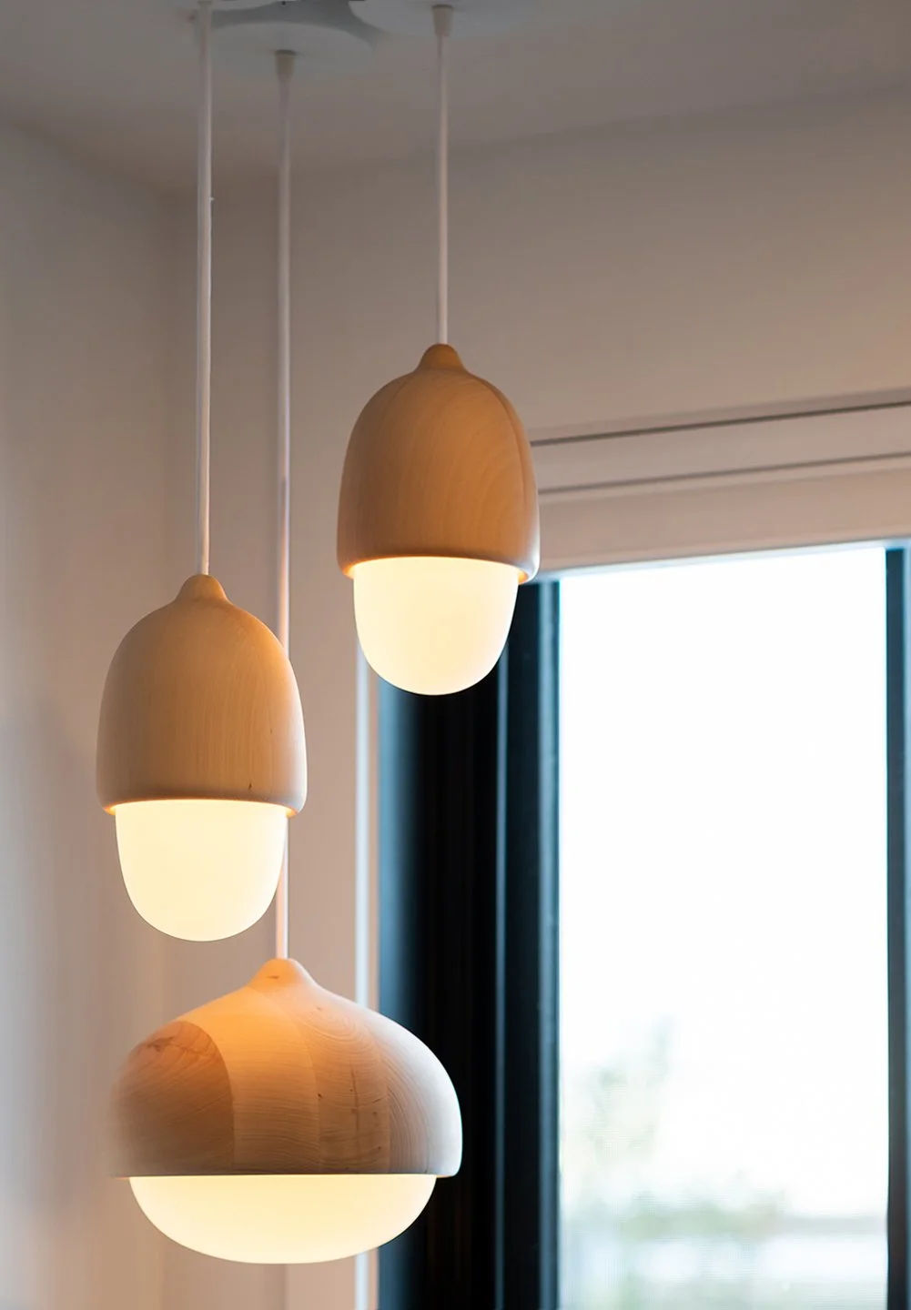 Three modern pendant lights with wooden and white shades hanging from the ceiling near a window with blinds. Seattle, Capitol Hill, Remodel.