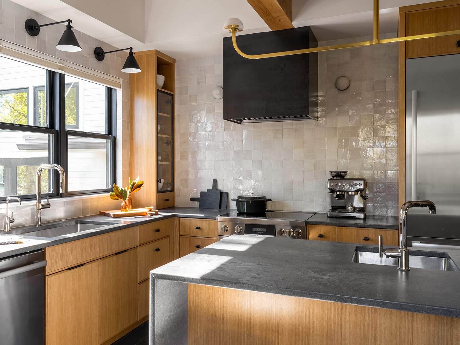 Modern kitchen with wooden cabinets, black countertops, stainless steel appliances, large window with view outside, and pendant lights. Bozeman, Montana, Remodel.