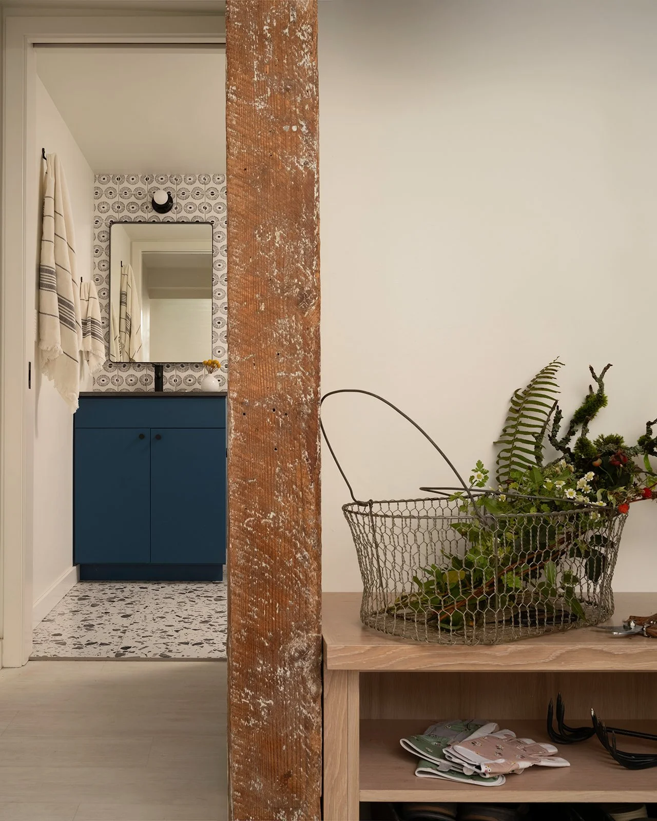 Interior of a home, showing a brown wooden beam, a cabinet with greenery, and a bathroom with a mirror and blue vanity.  Seattle, Queen Anne, Remodel.