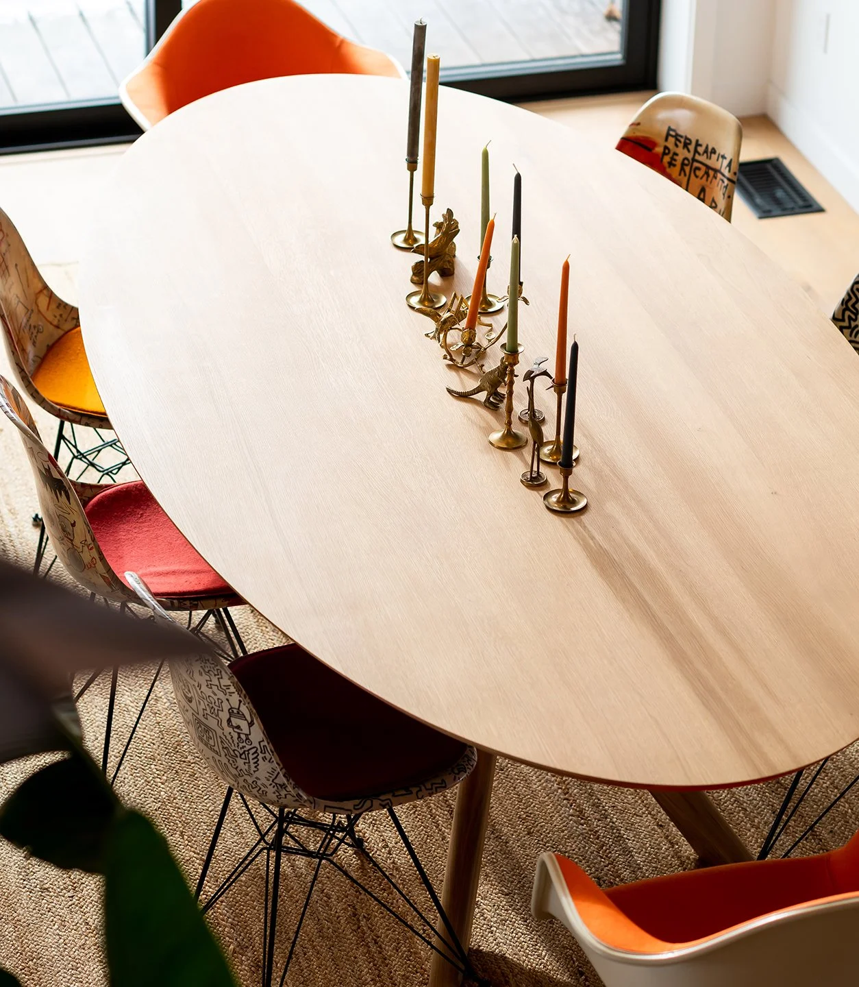 Wooden dining table with colorful candles and dinosaur-shaped candle holders, surrounded by mismatched chairs with various patterns and colors. Seattle, Capitol Hill, Remodel.