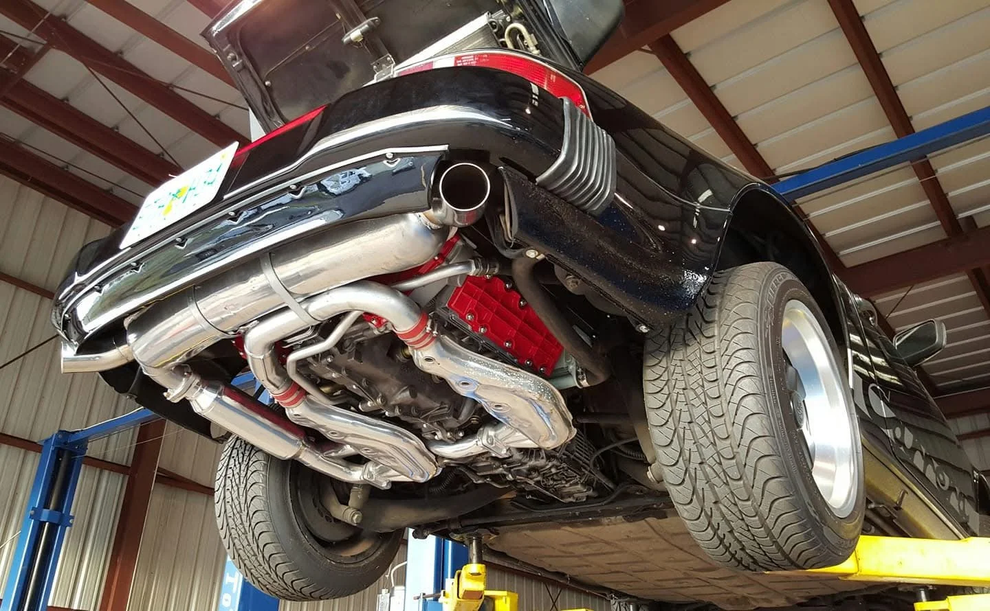 Car on lift showing exhaust system, rear bumper, and tire in a garage.