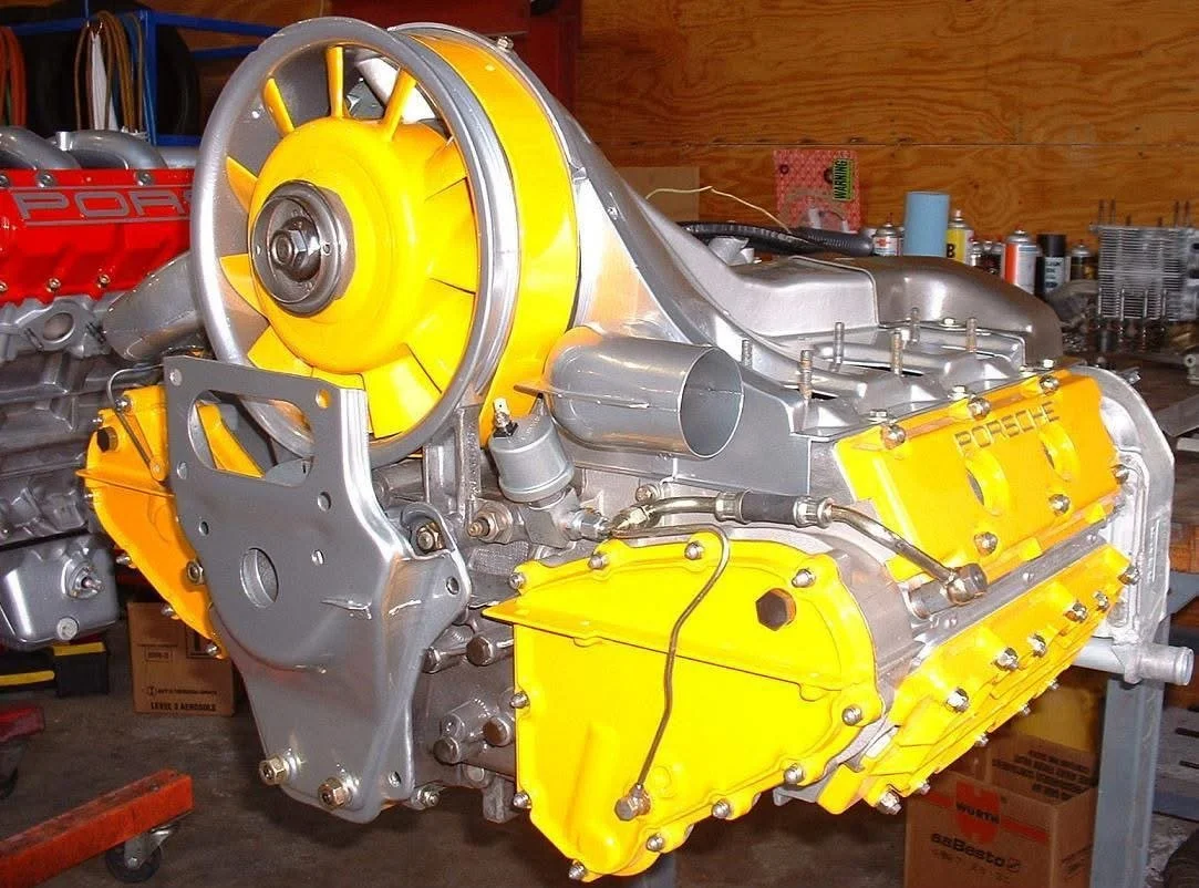 Porsche air-cooled engine, yellow fan shroud, partial view of another red engine in the background.