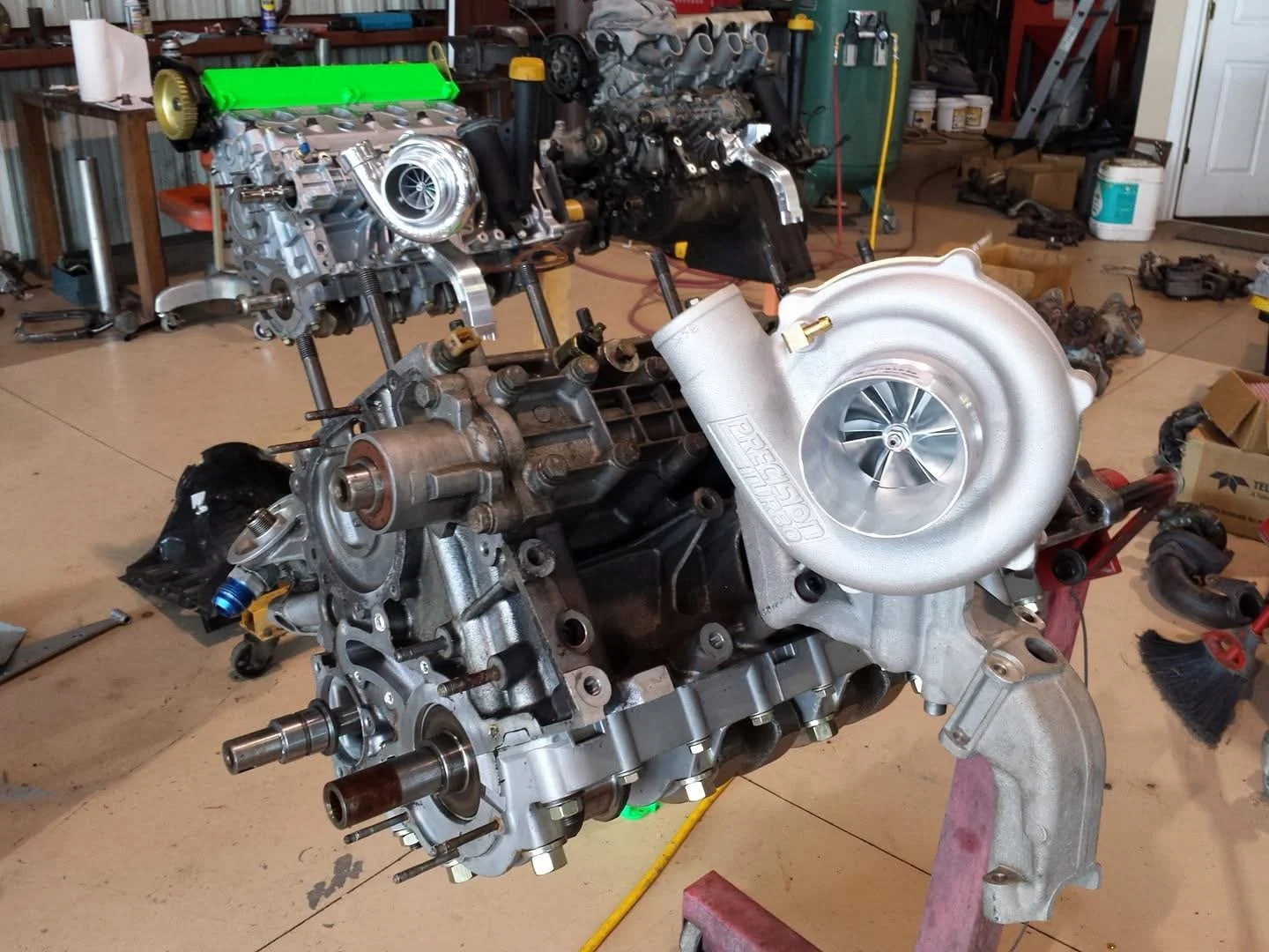 A detailed view of a car engine with a turbocharger attached, placed on a stand in an automotive workshop.