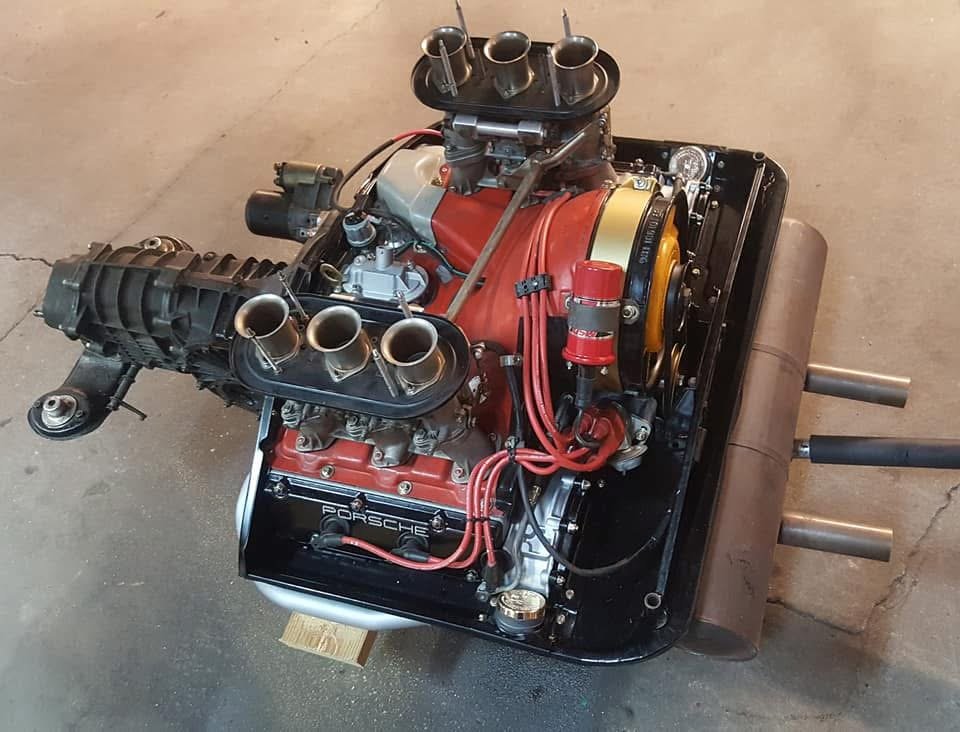 High-performance Porsche engine on the floor, featuring carburetors, exhaust pipes, and ignition wires.