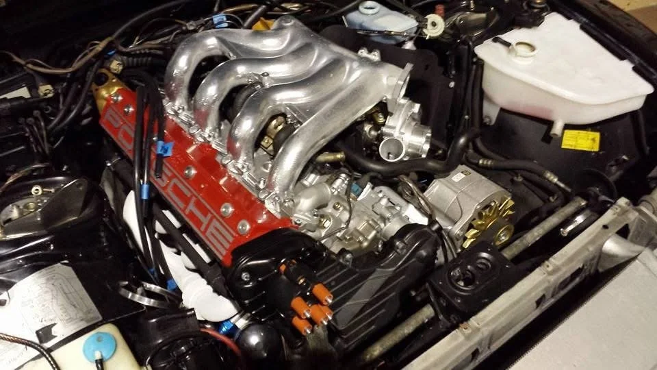 Porsche engine in a car with visible intake manifold and components.