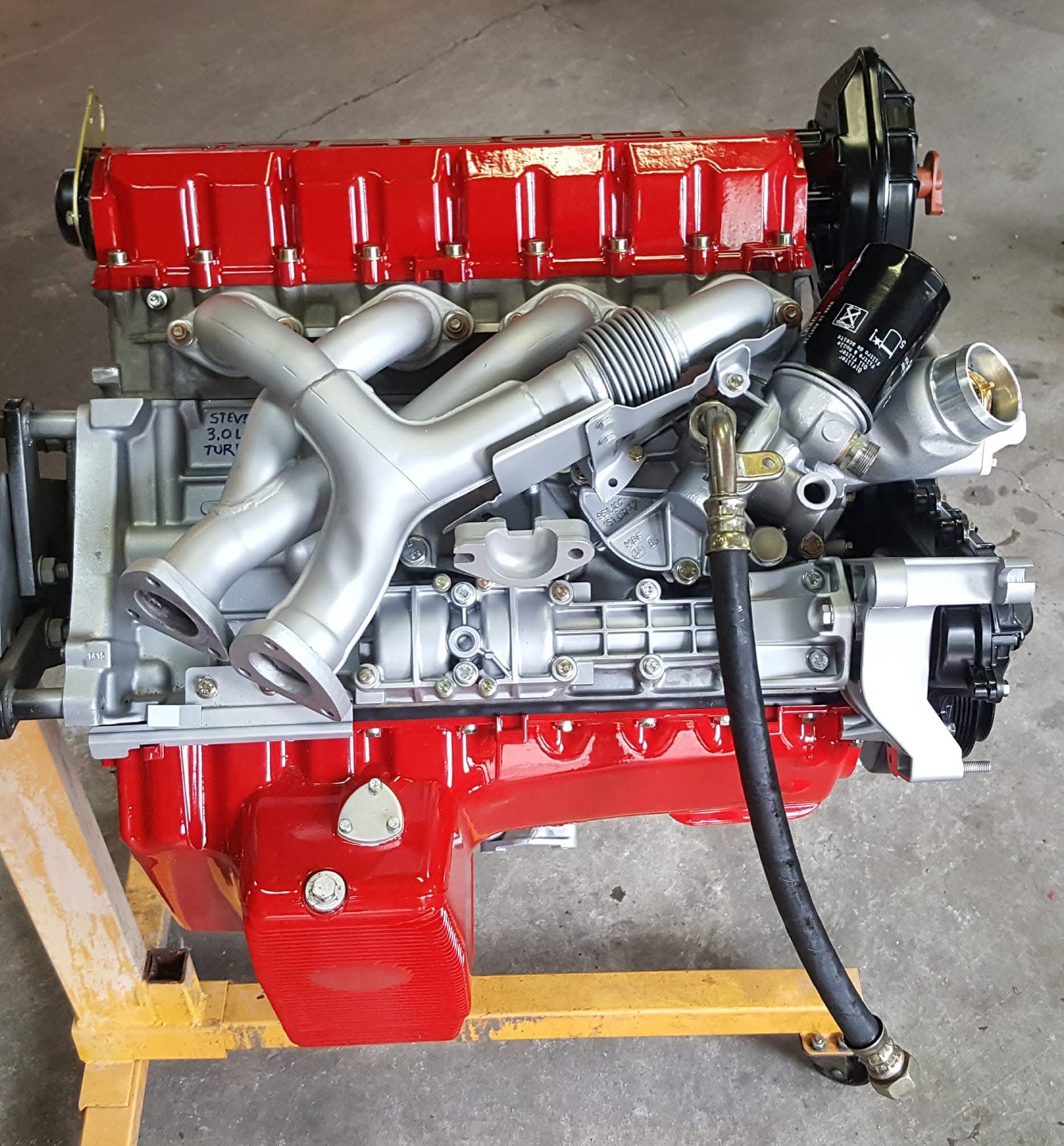 A detailed view of a car engine with a red valve cover and metallic components.