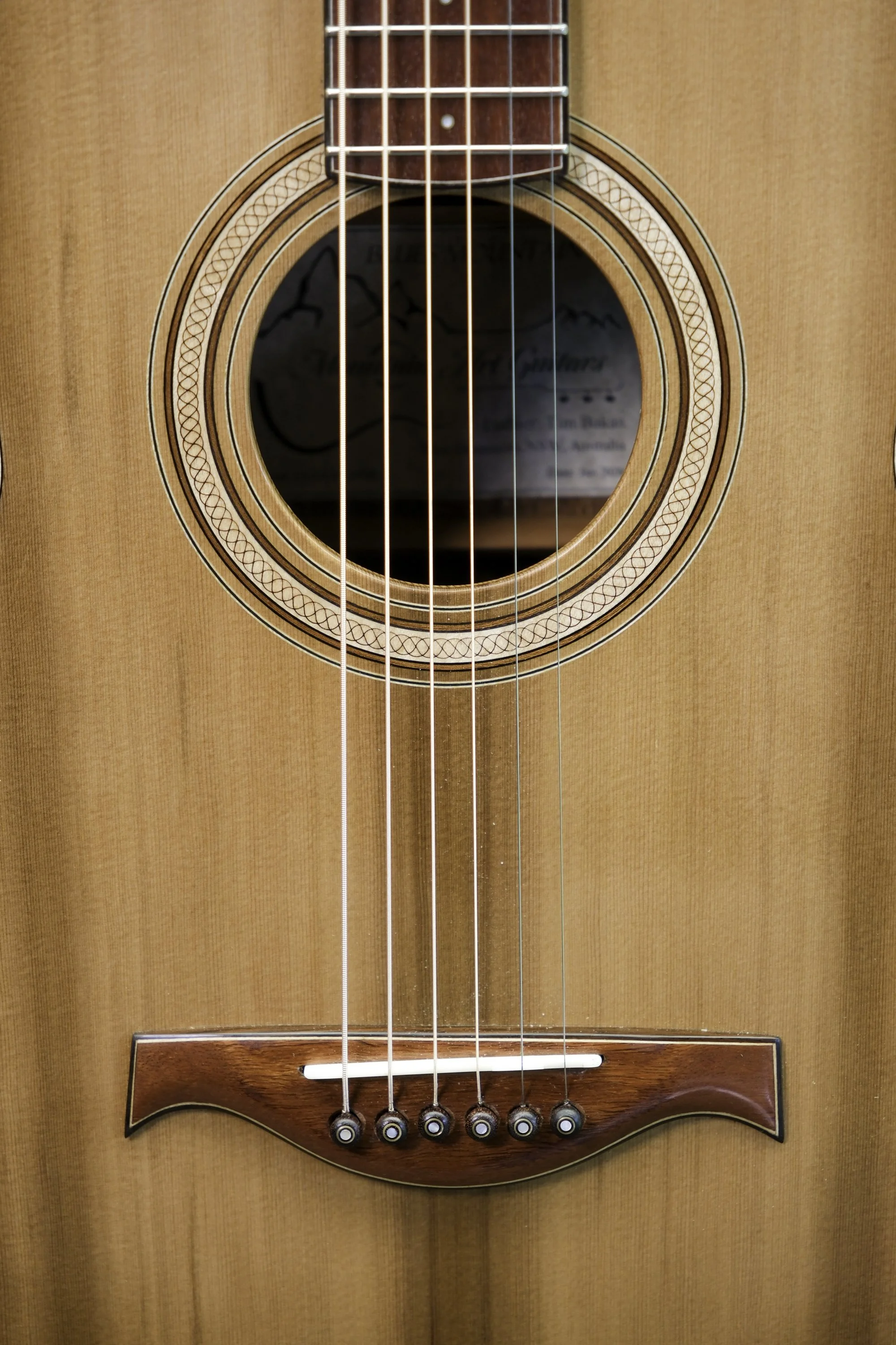 Close-up image of an acoustic guitar's soundhole, strings, bridge, and rosette in natural wood finish.