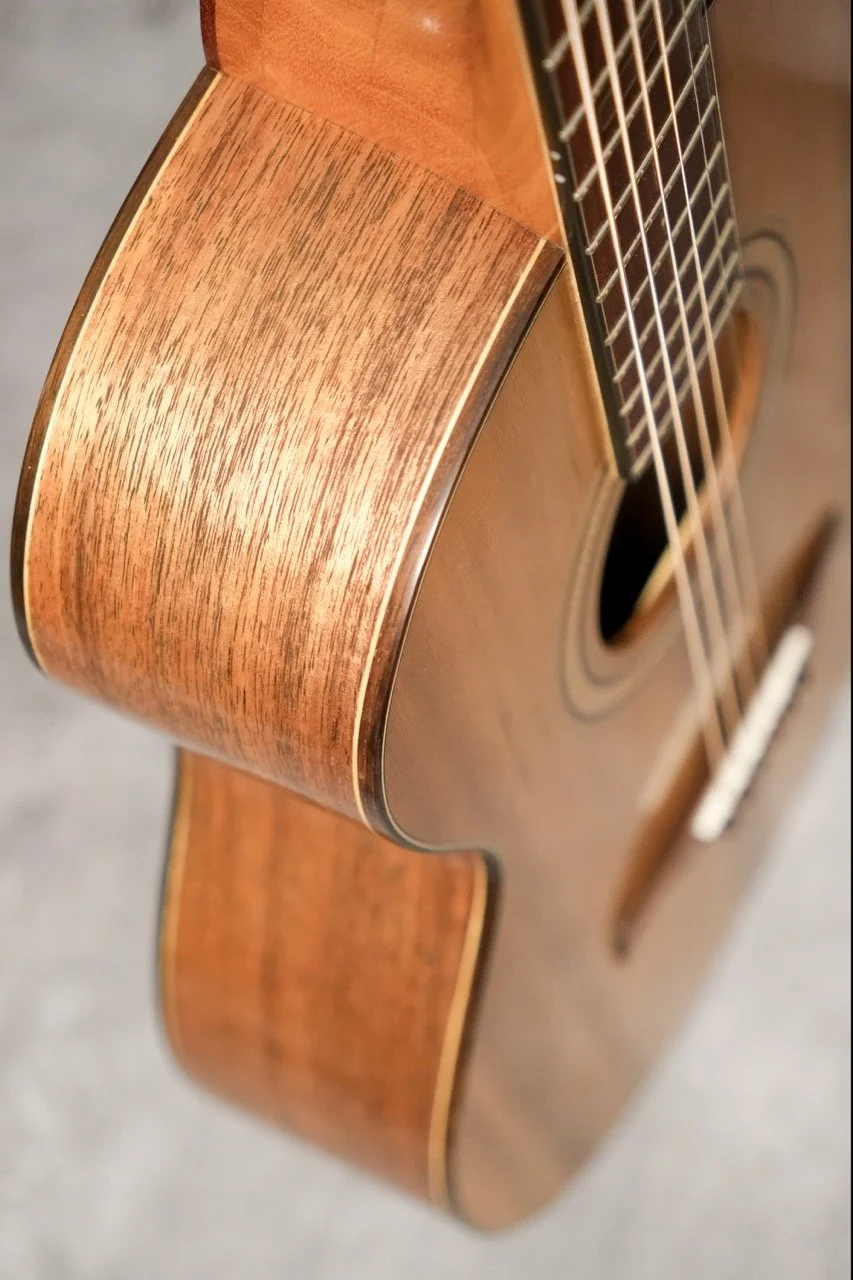 Close-up of an acoustic guitar's body and fretboard, showing wood grain and strings.
