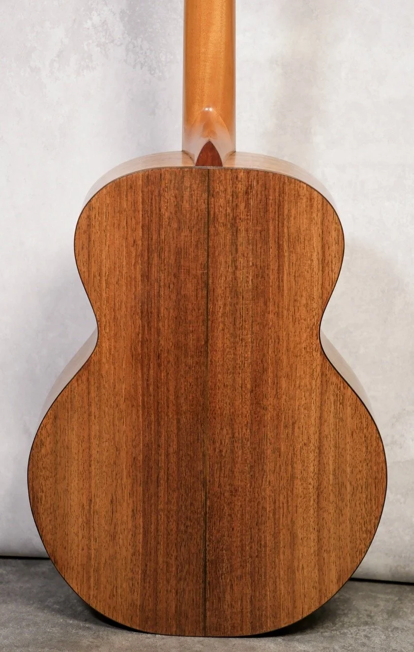 Back of a wooden acoustic guitar showing its rounded body and neck against a neutral background.