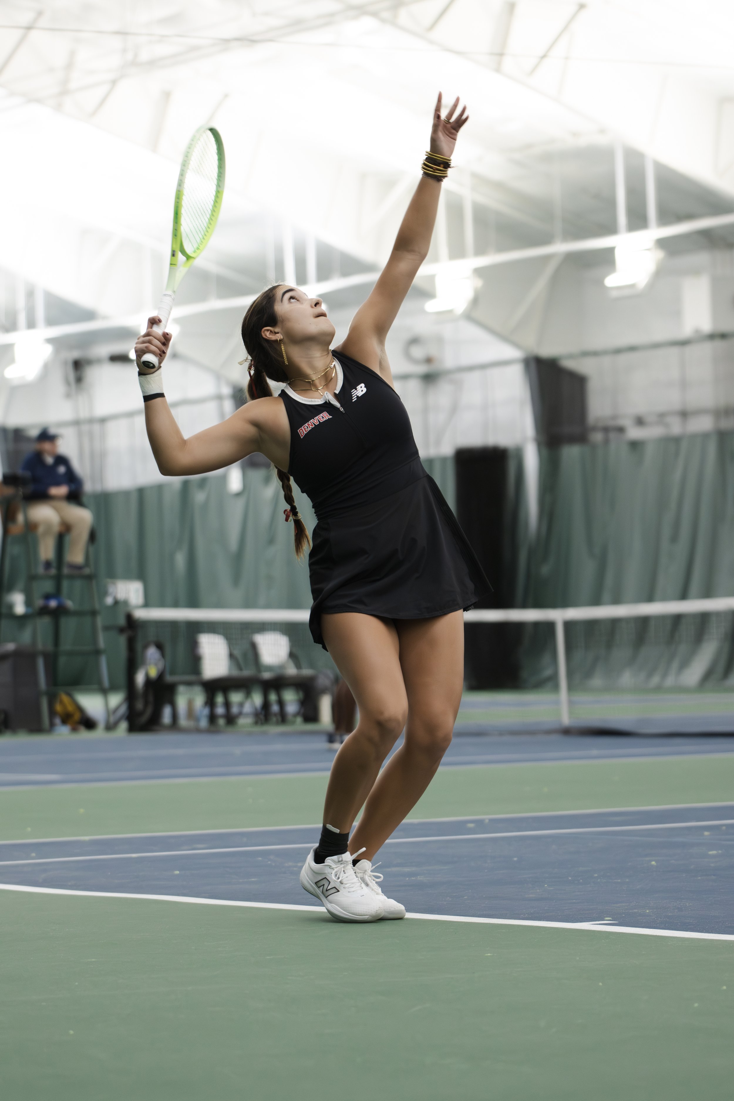 Female tennis player in black sportswear serving on an indoor tennis court.