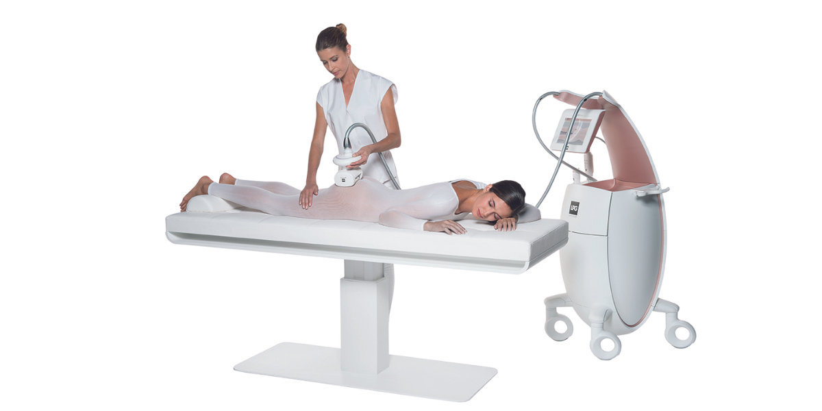 A woman lying face down on an endermologie treatment table while a therapist performs a lymphatic drainage massage
