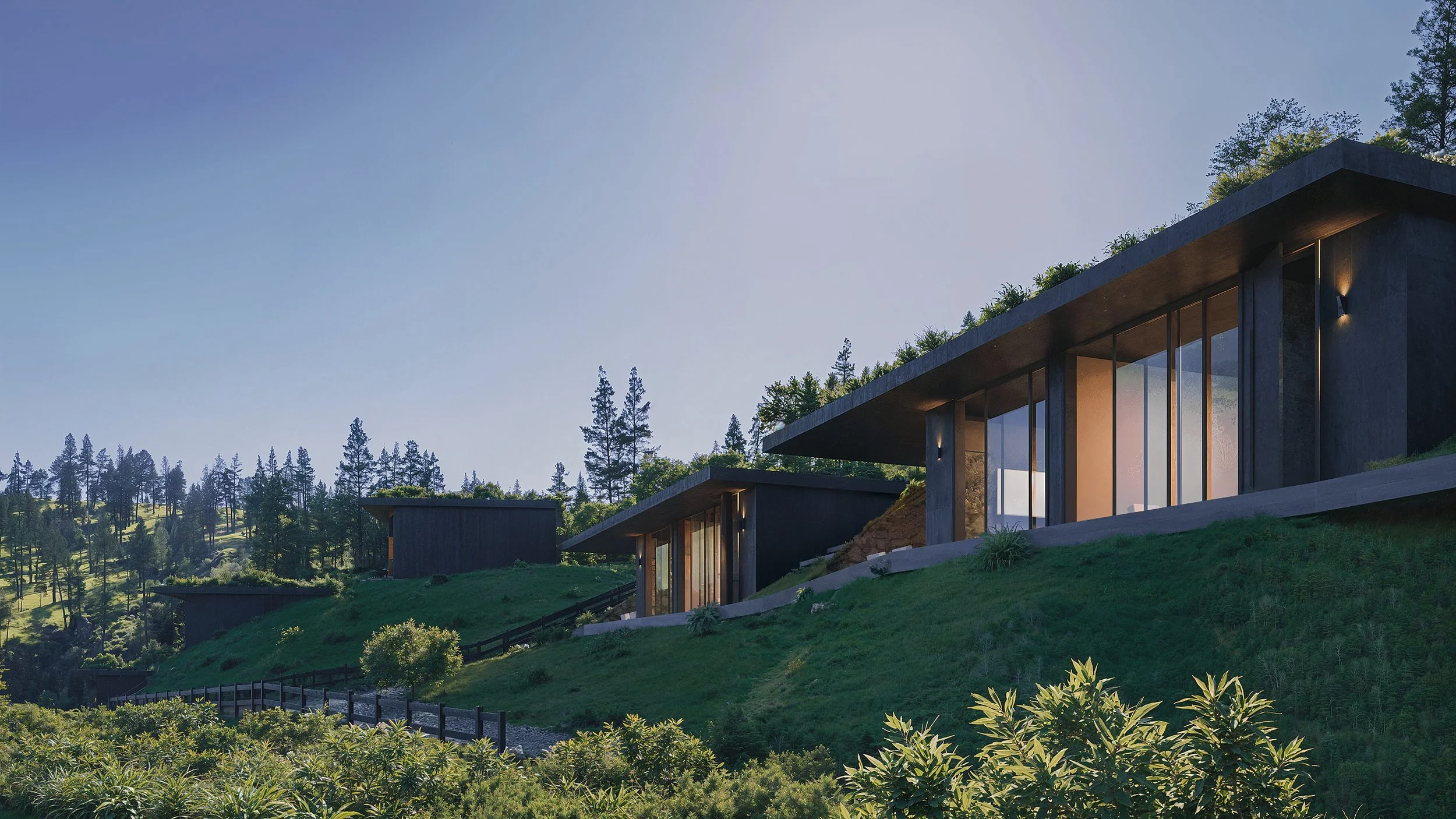 Modern houses with large glass windows on a green hillside surrounded by trees under a clear blue sky