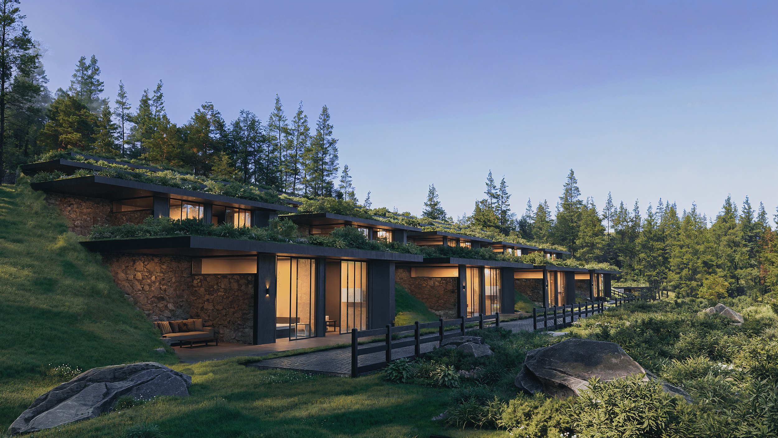 Modern multi-level house built into a hillside surrounded by trees, with large glass windows and outdoor seating, during daytime.