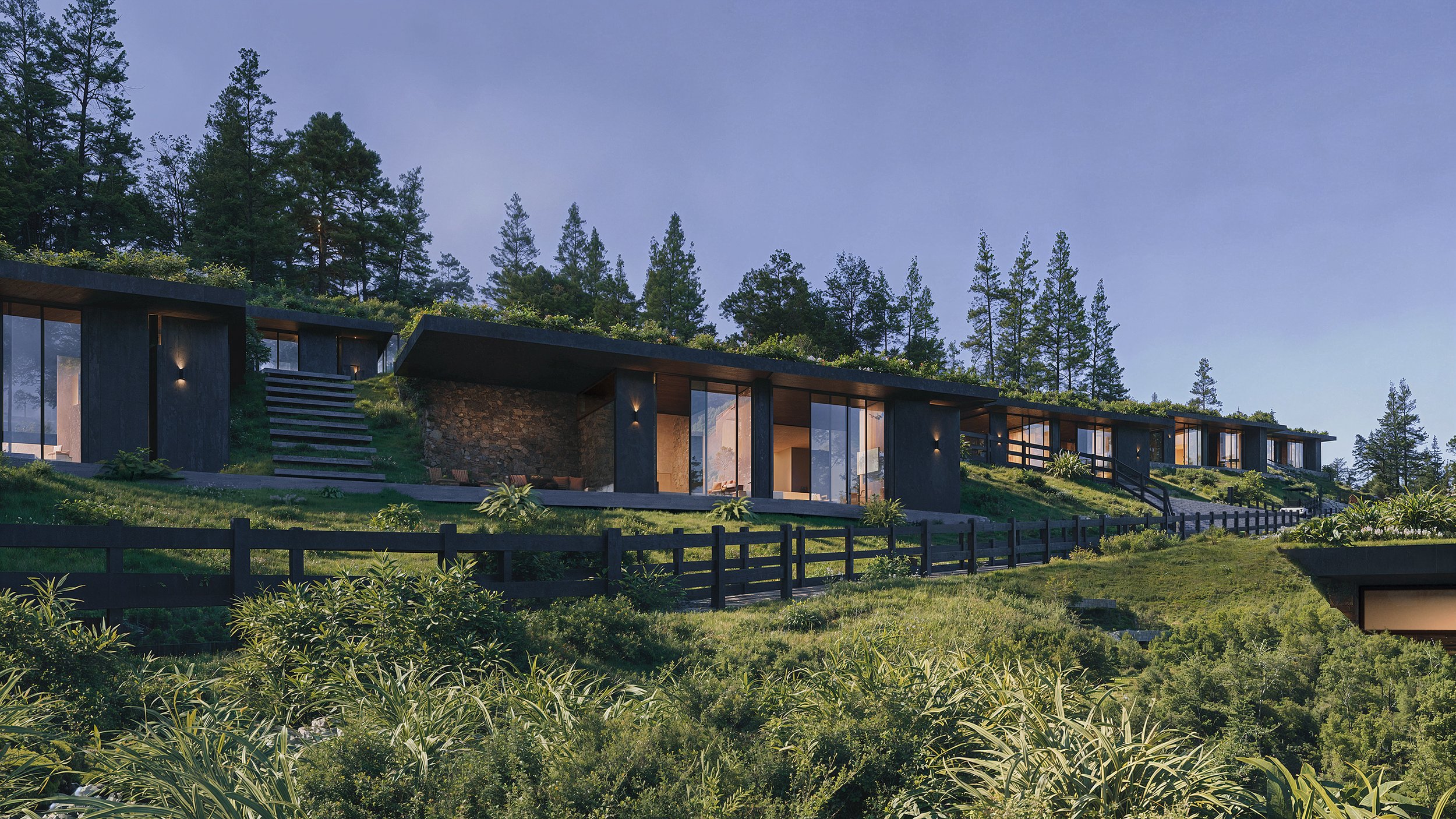 Modern hillside house with large glass windows, surrounded by trees and greenery under a clear sky.