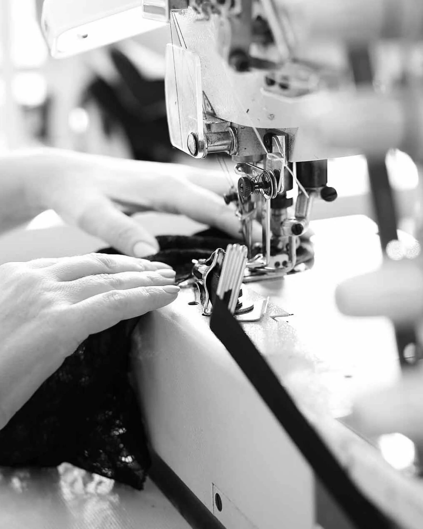 Close-up of hands guiding fabric under a sewing machine needle in black and white.