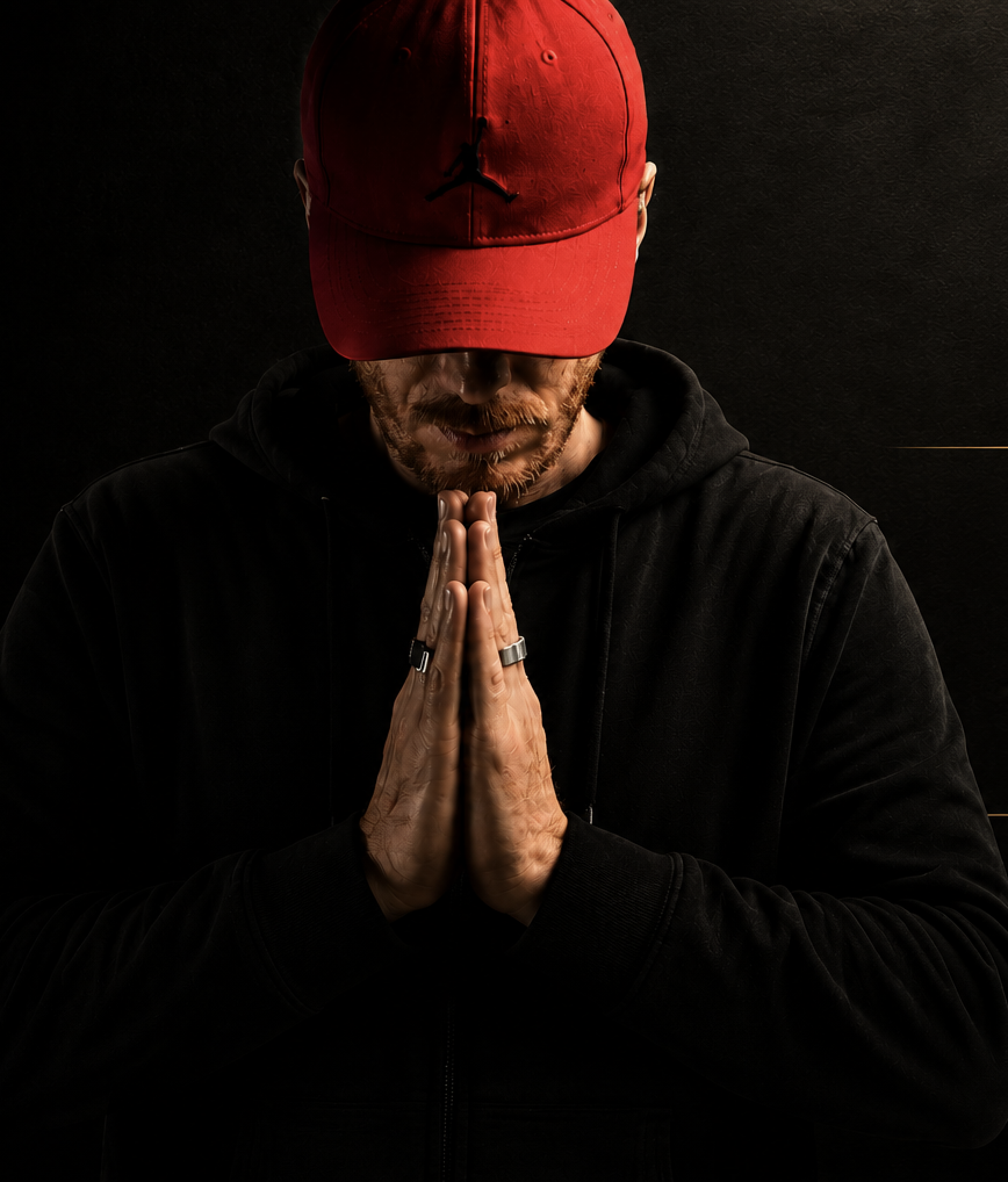 Persona con cappello rosso con il logo Jumpman, testa chinata, mani giunte in preghiera, sfondo nero