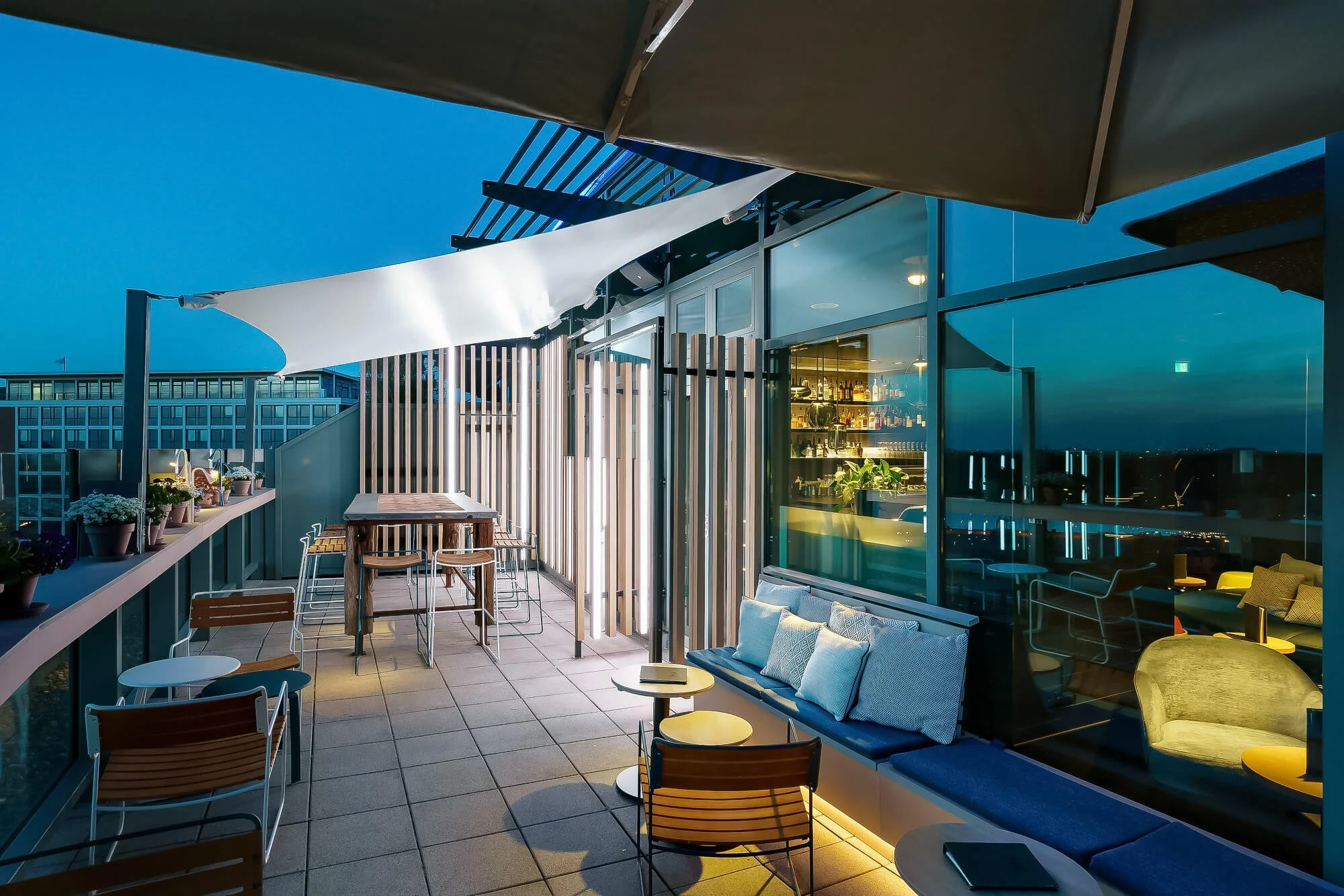 Outdoor terrace with tables, bar stools, and urban panorama at twilight – photo by Milan Istvan