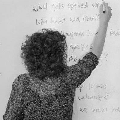 Person writing on a whiteboard with curly hair and patterned shirt.