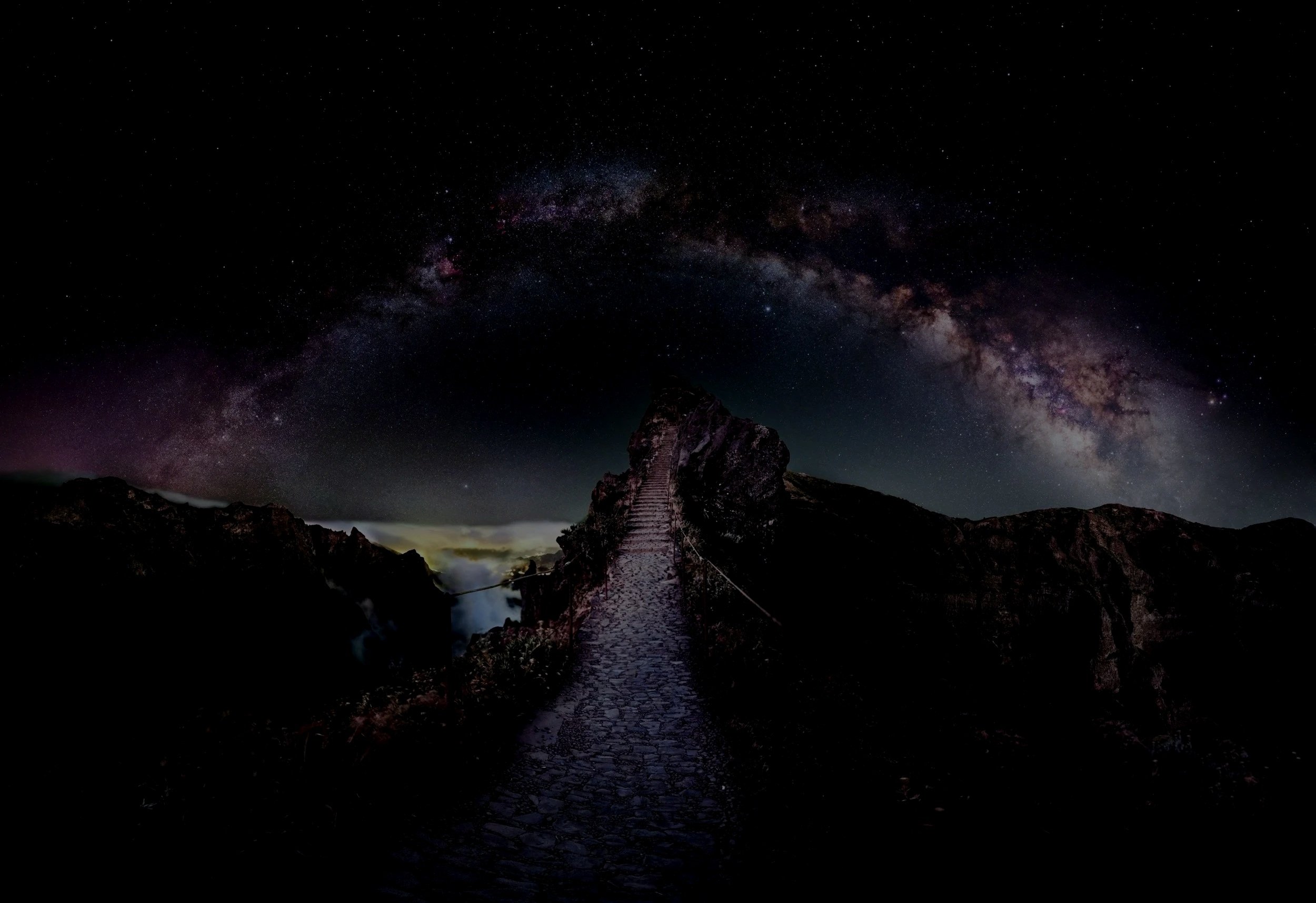 A stone pathway leading up a mountain, with a starry night sky and the Milky Way galaxy overhead.