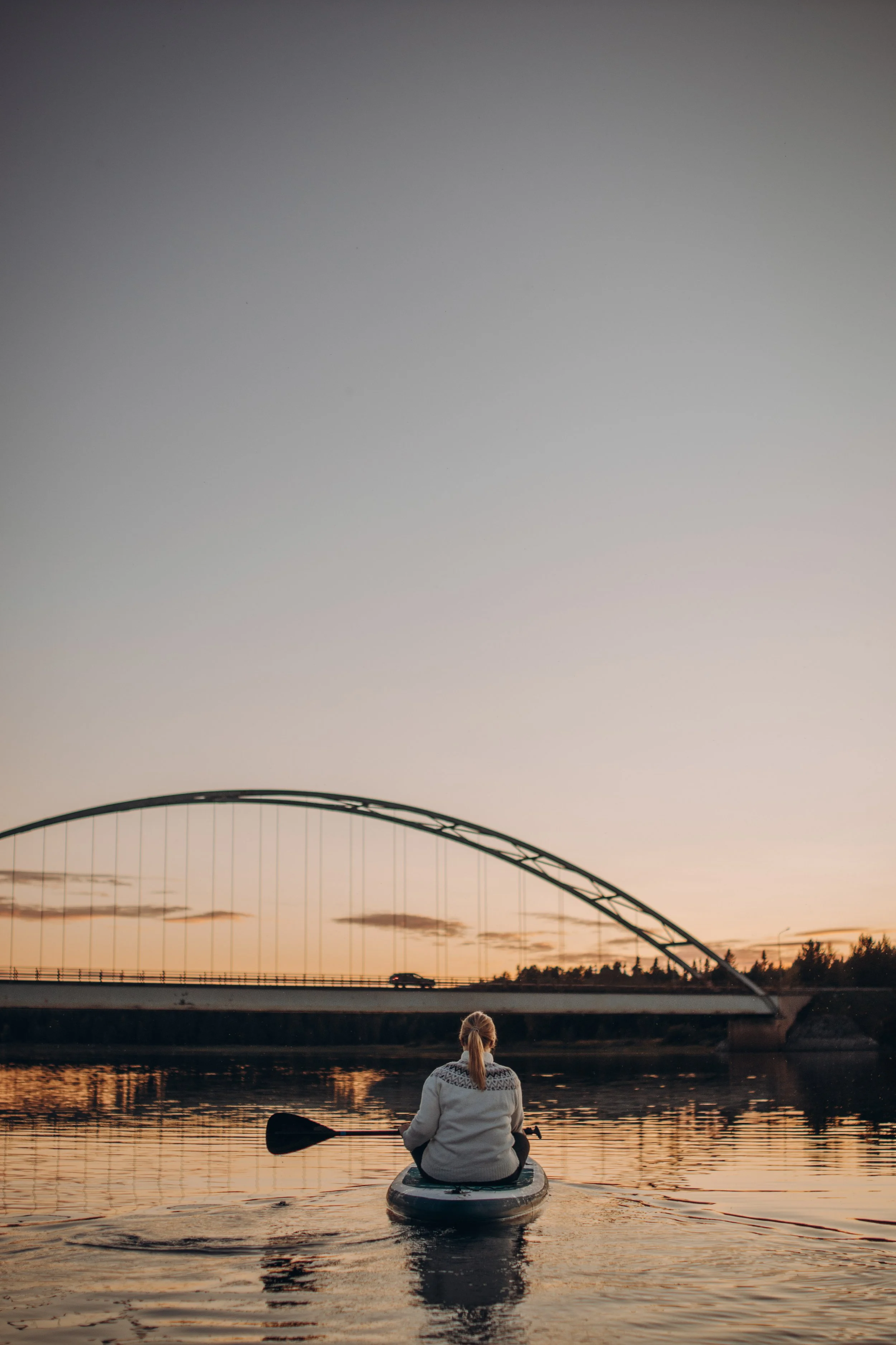 Person paddlar på en flod vid solnedgång, med en bro i bakgrunden.