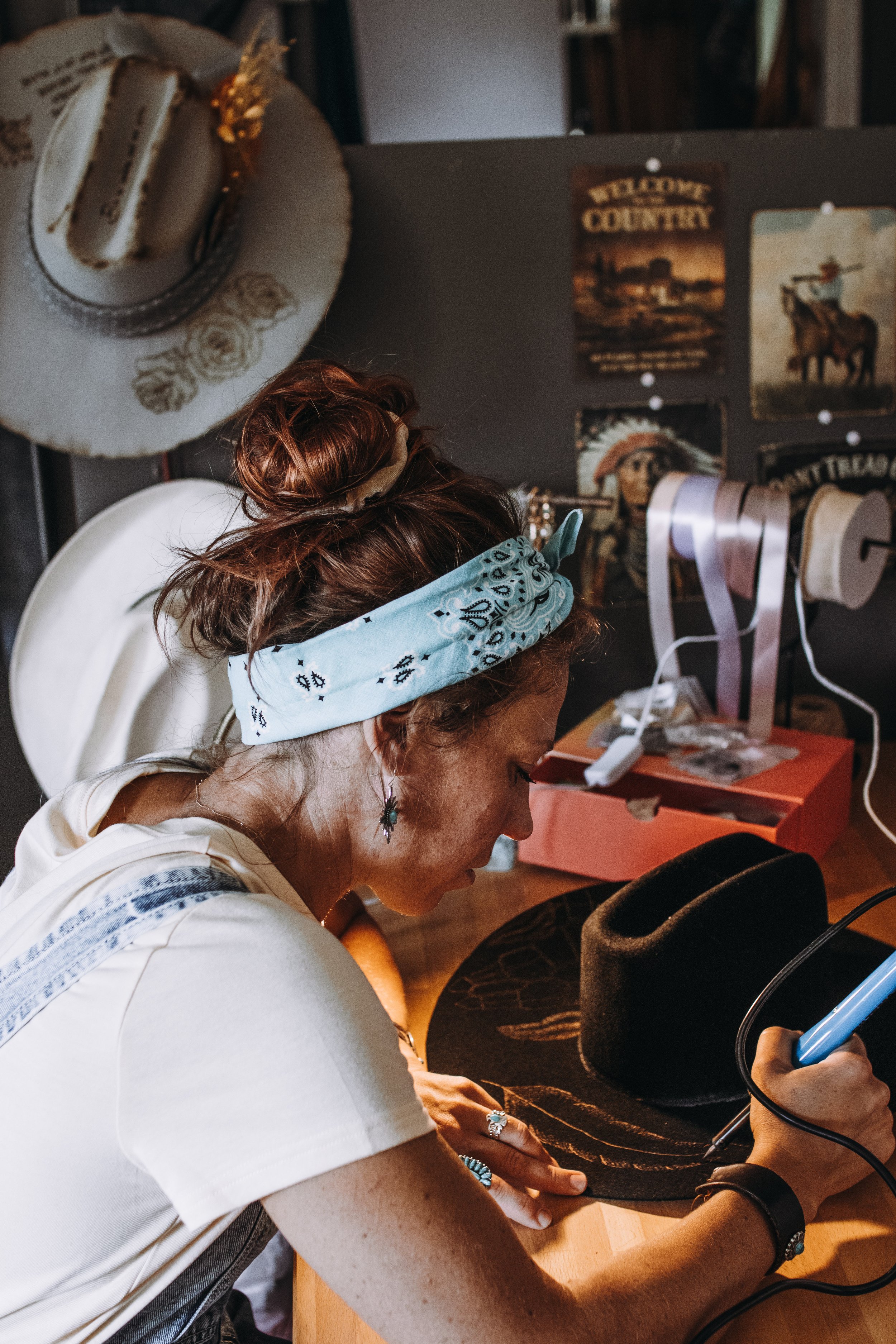 Kvinna i vitt T-shirt med blått bandana i håret använder en varm luftpistol för att forma en svart hatt