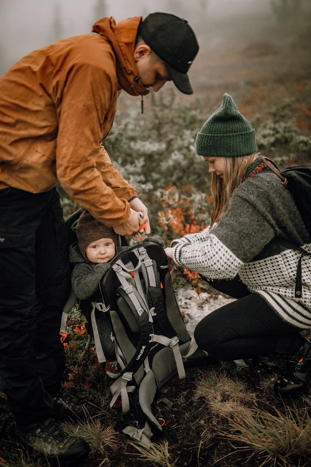 Ett par på fjällvandring hjälps åt att packa upp väskan med en liten bebis i stolen på ryggsäcken