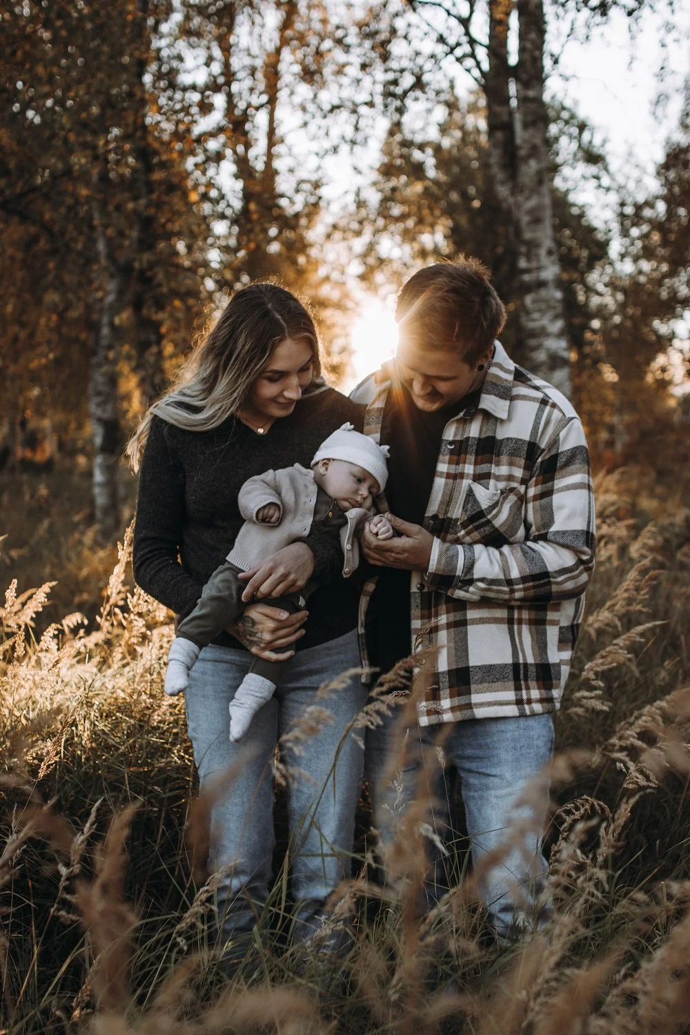 Familj med en man, en kvinna och ett barn i ett fält med höstlöv, solen gående ner i bakgrunden.