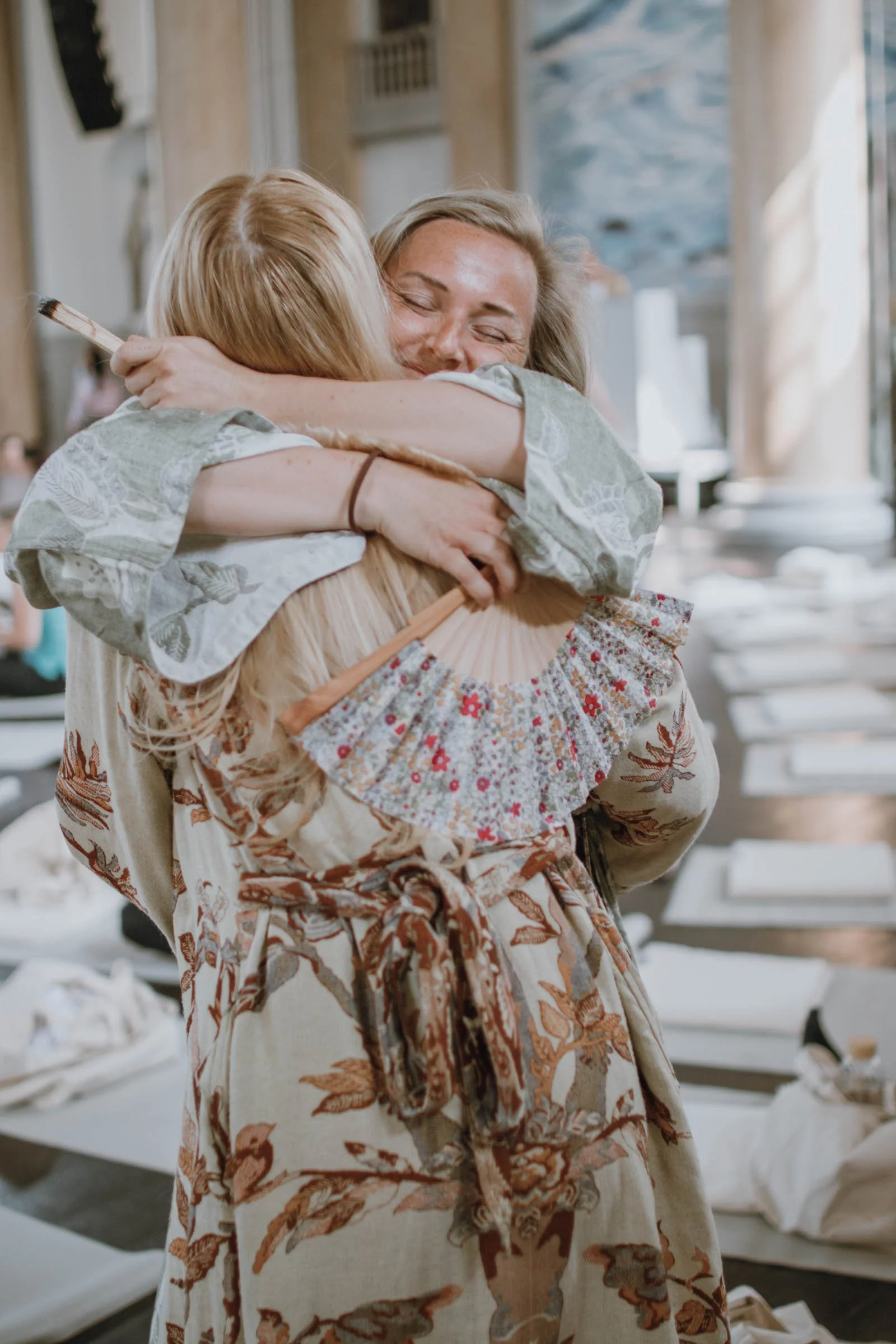 Två personer i handgjorda kläder omfamnar varandra i ett inomhusmiljö, glada och leende.