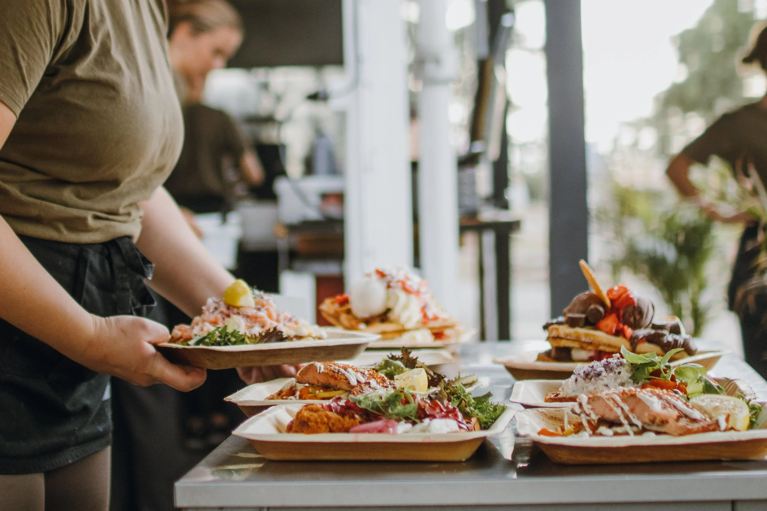 Person som håller i en tallrik med mat, flera tallrikar med olika maträtter och desserter på ett bord.