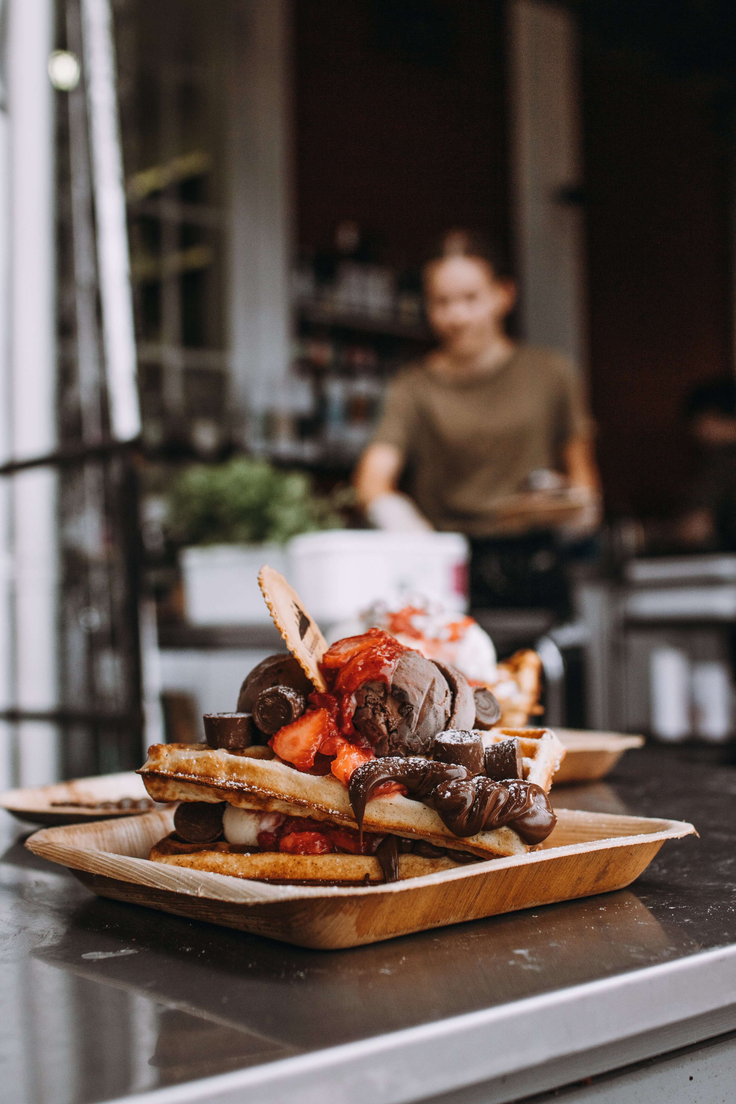 En tallrik med belgisk våffla toppad med chokladsås, jordgubbar och glass, på ett serveringsfat.