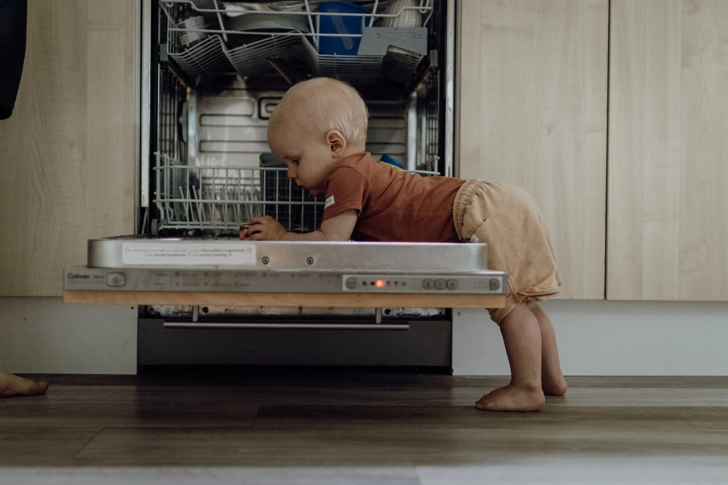 Ett barn som kryper in i diskmaskinen i ett kök.